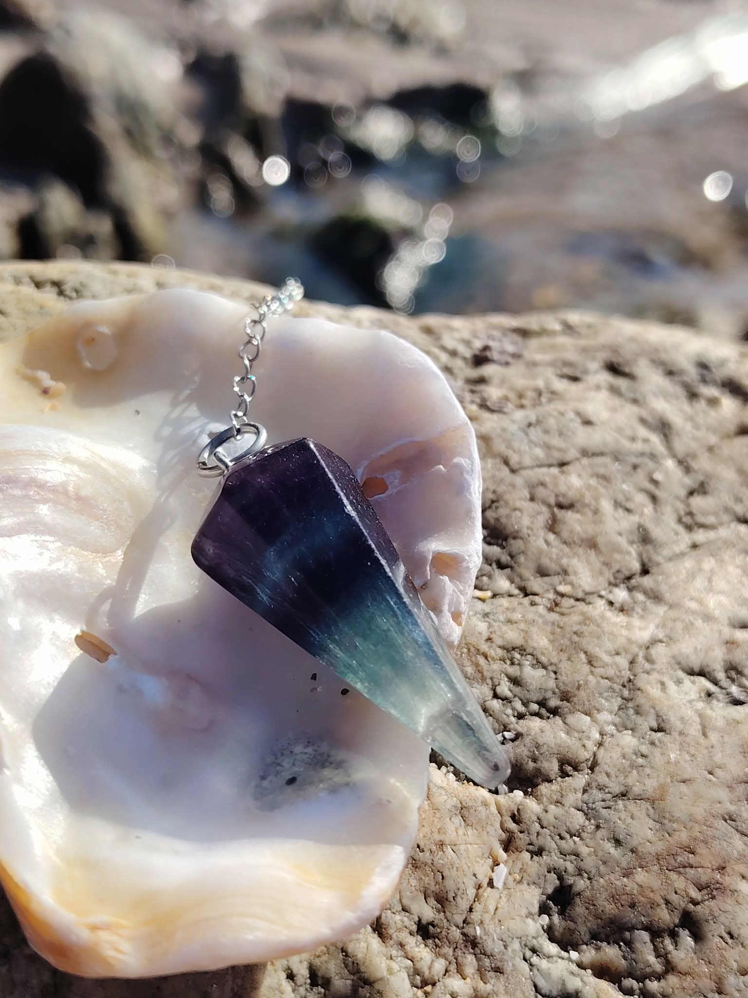 Pendule en fluorite présenté comme outil de divination sur un décor minéral, dans une ambiance douce et mystique évoquant clarté mentale, intuition et recentrage.