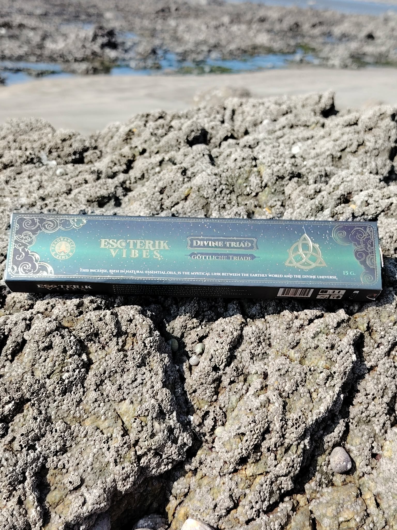 Boîte d’encens masala Triade 15 g Fragrance et Sens, posée sur les rochers face à l’eau en Bretagne, dans une ambiance spirituelle évoquant harmonie, recentrage et élévation.