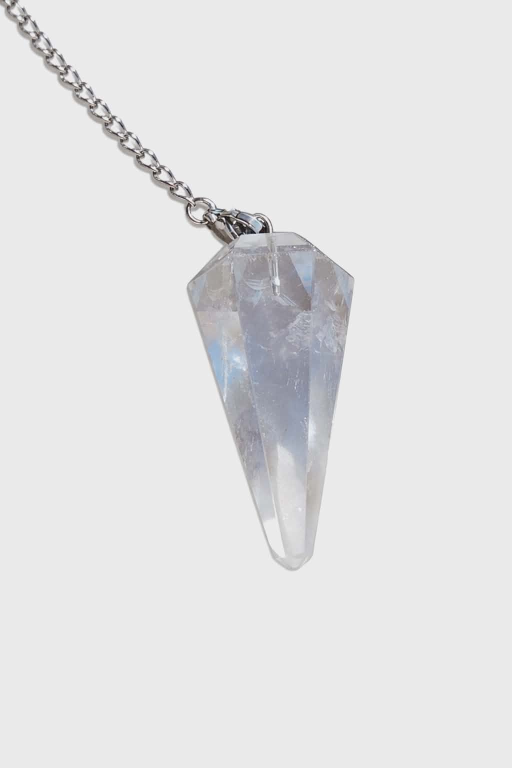 Pendule en cristal de roche transparent sur fond blanc, avec chaîne argentée, évoquant clarté mentale, intuition et recentrage.