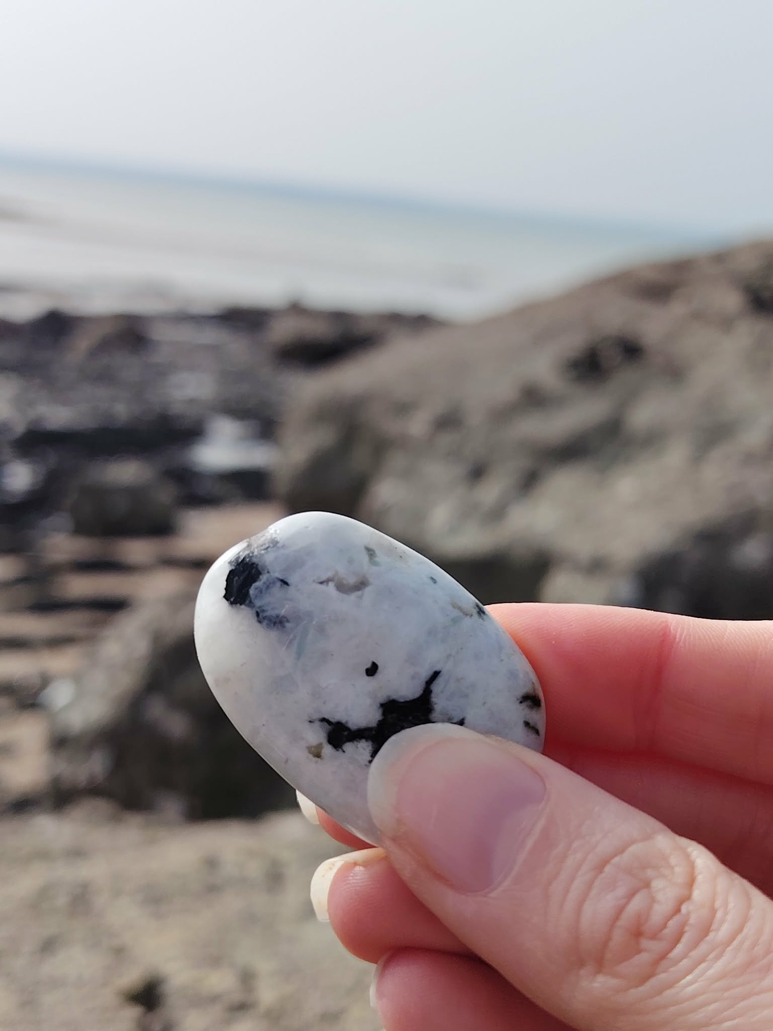Galet de péristérite tenu en main face à la mer en Bretagne, pierre de lune arc-en-ciel évoquant la délicatesse, l’écoute de soi et la tranquillité intérieure.