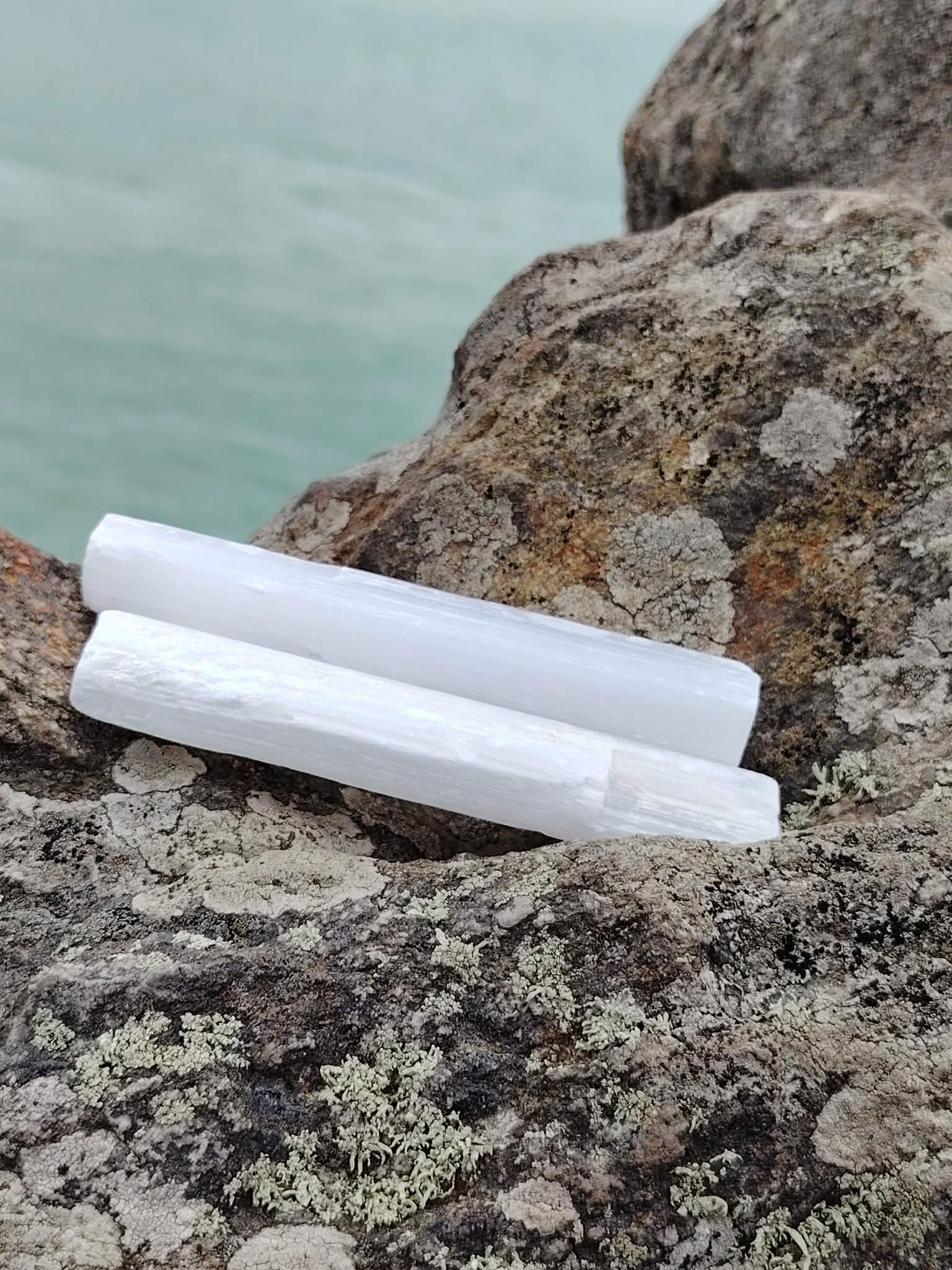 Baguette de sélénite sur rochers en Bretagne face à la mer, pierre blanche naturelle, calme mental et purification subtile.