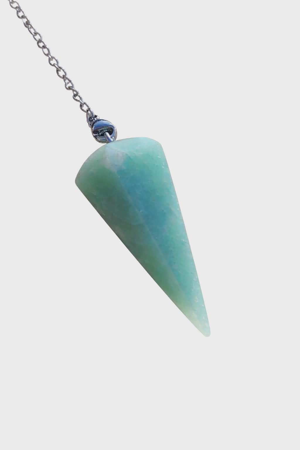 Pendule en amazonite bleu-vert sur fond blanc, chaîne argentée visible, image épurée évoquant douceur, clarté intérieure et harmonie.