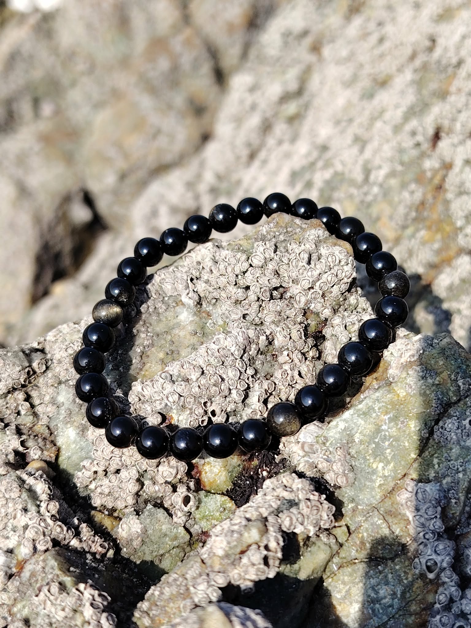Bracelet obsidienne dorée 6 mm sur roches claires en Bretagne, reflet doré discret, aplomb, volonté et enracinement