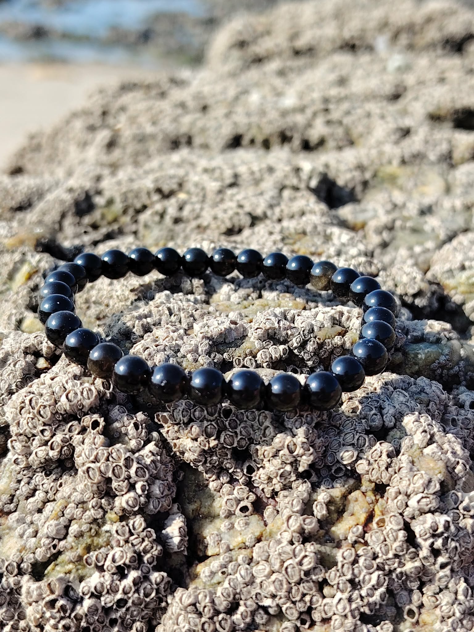 Bracelet obsidienne dorée 6 mm sur rochers marins en Bretagne, perles sombres brillantes, discernement et stabilité intérieure