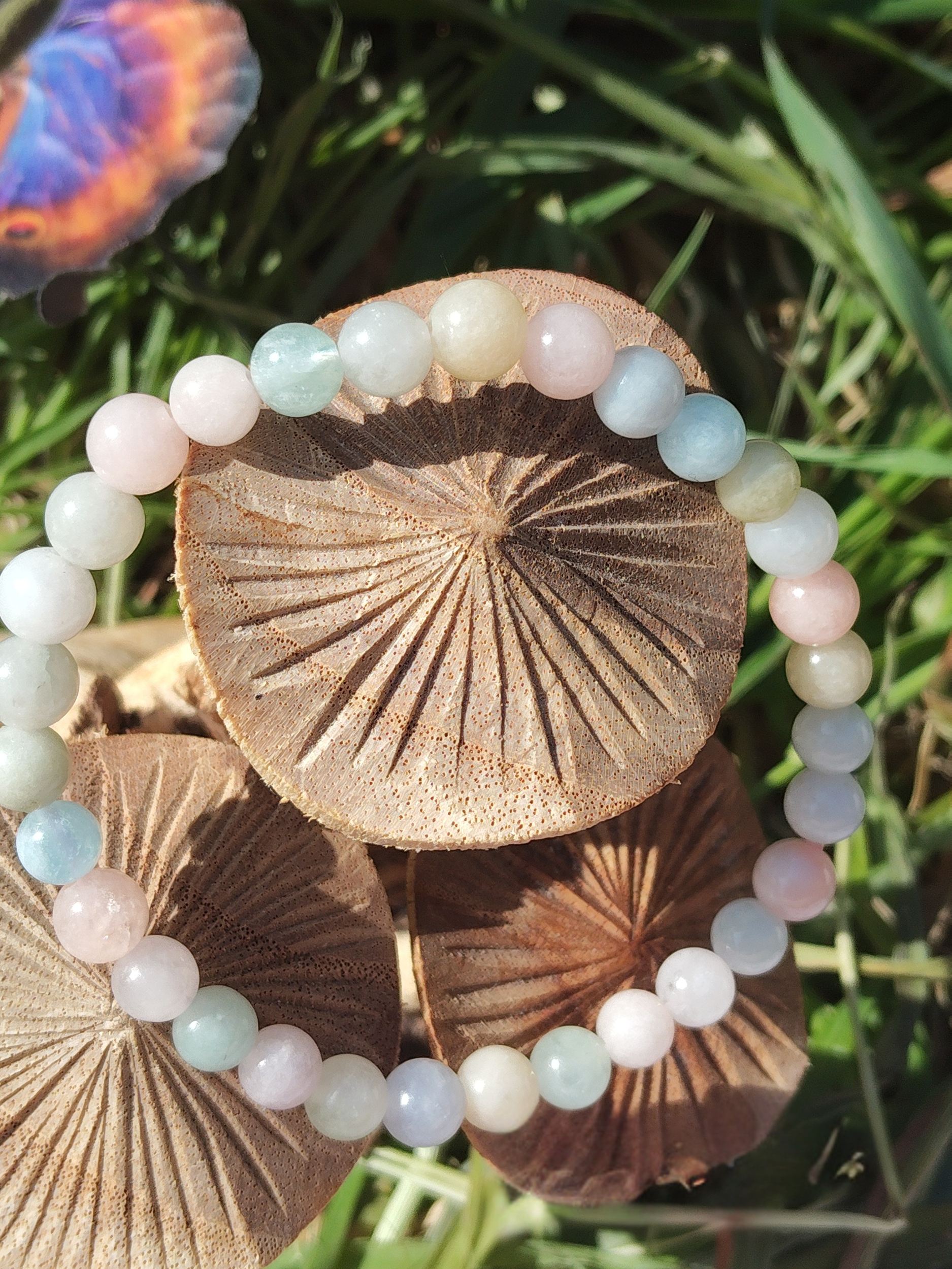 Bracelet Morganite 6 mm posé sur champignons en bois avec herbe verte, perles pastel rose, bleu et crème, bijou en pierre naturelle évoquant la douceur relationnelle, la délicatesse et la stabilité affective.