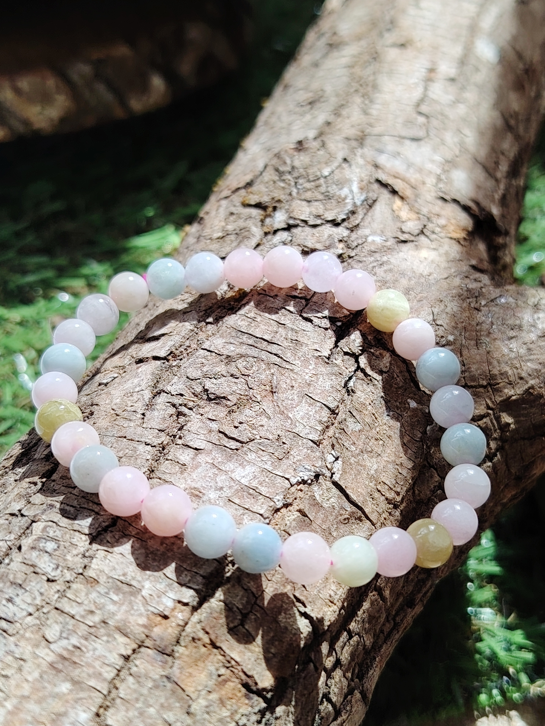 Bracelet Morganite 6 mm posé sur tronc, perles pastel lumineuses en décor naturel, bijou en pierre naturelle associé à la tendresse, au calme émotionnel et à la douceur intérieure.