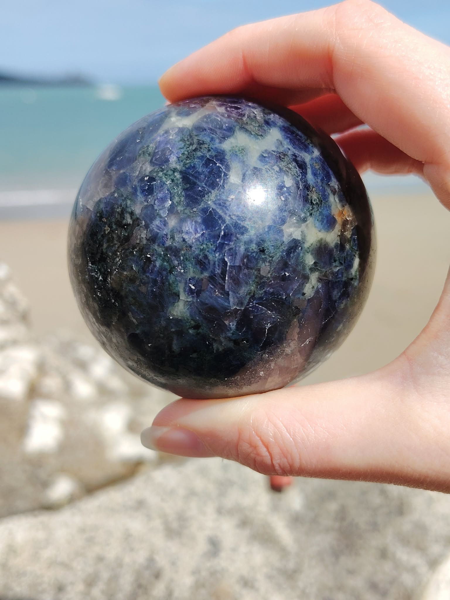 Sphère iolite ou cordiérite tenue entre les doigts sur la plage en Bretagne, pierre bleu profond aux reflets minéraux, confiance en soi et calme intérieur.