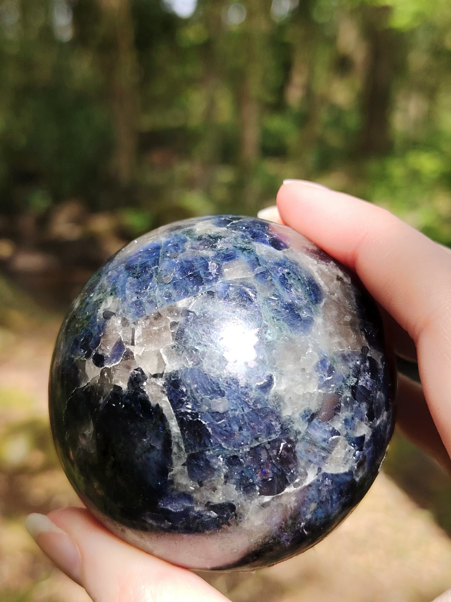 Sphère iolite ou cordiérite tenue en main en forêt en Bretagne, pierre bleu gris polie aux marbrures naturelles, recentrage et vision plus claire.