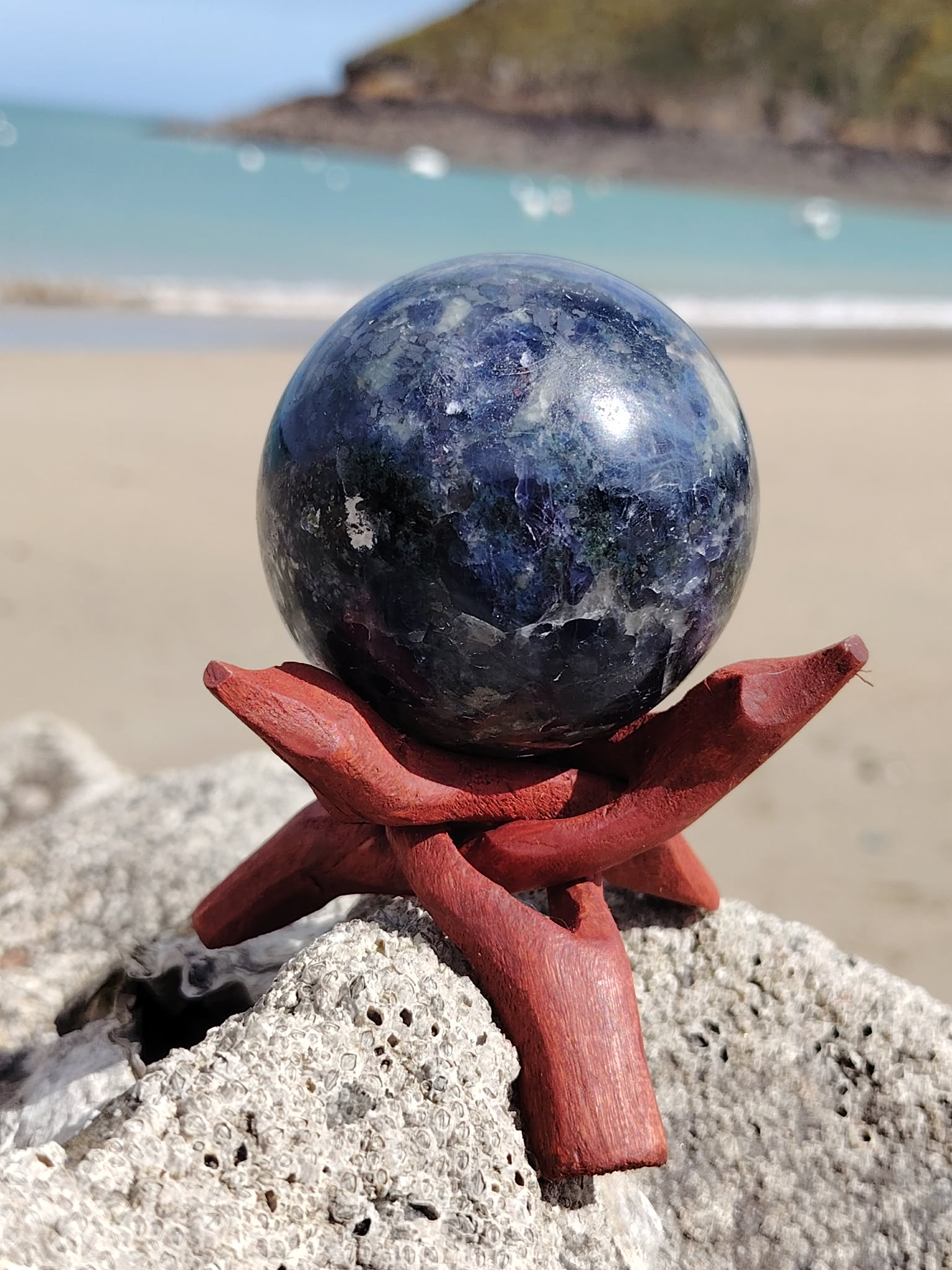 Sphère iolite ou cordiérite photographiée sur rocher coquillé en Bretagne au bord de mer, pierre bleu gris naturelle, harmonie intérieure et créativité fluide.