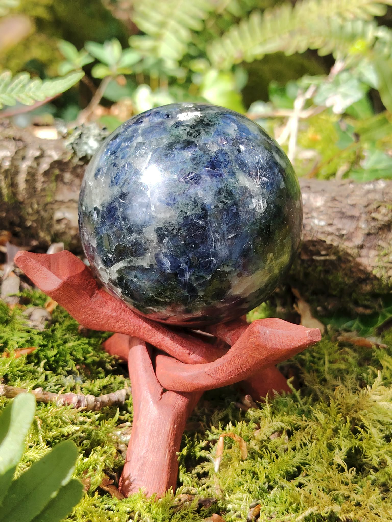 Sphère iolite ou cordiérite sur rondin de bois en forêt en Bretagne avec pomme de pin, pierre bleu gris polie, clarté intérieure et inspiration.