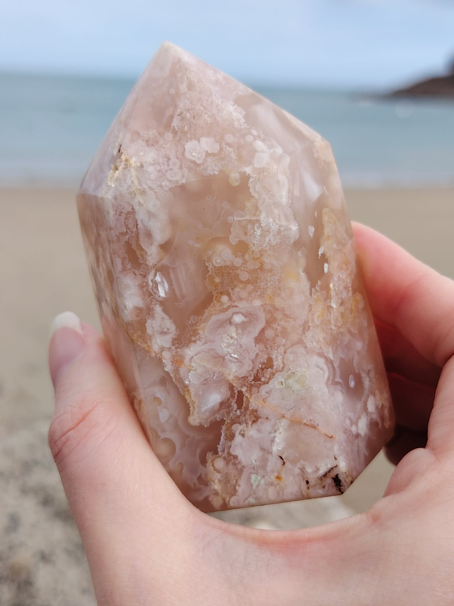 Pointe agate fleur de cerisier tenue en main au bord de mer en Bretagne, nuances beige rosé et dessins floraux, calme du cœur et confiance en soi.