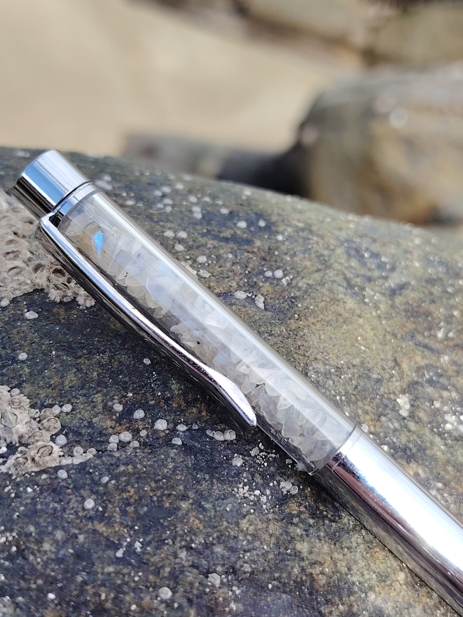 Stylo en Labradorite photographié sur roche marine texturée, reflets métallisés bleu acier, soutien à l’intuition et à la clarté d’esprit.