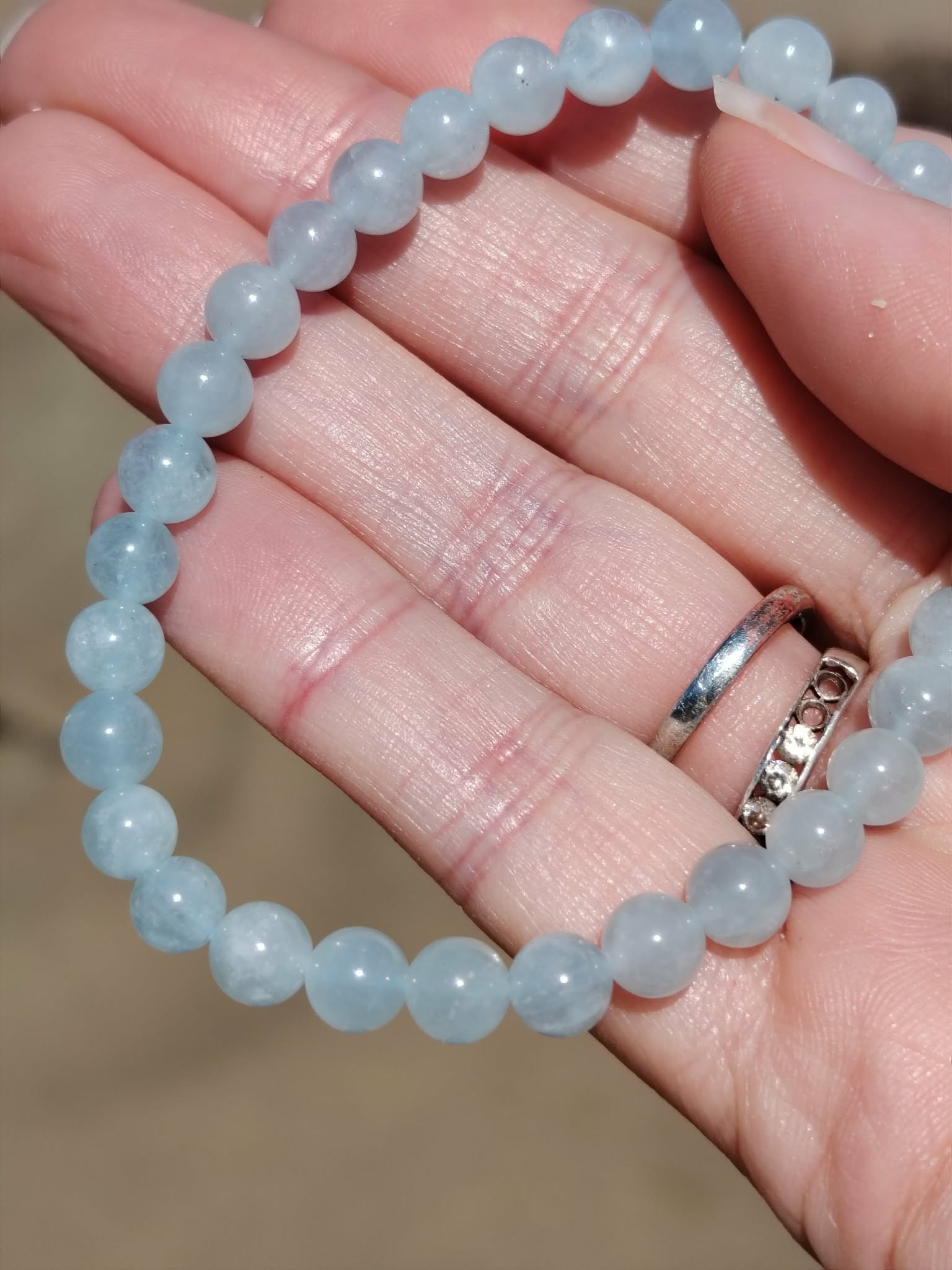 Bracelet Aigue-Marine 6 mm sur pierre en bord de plage, perles bleu pastel, fluidité émotionnelle et expression authentique.