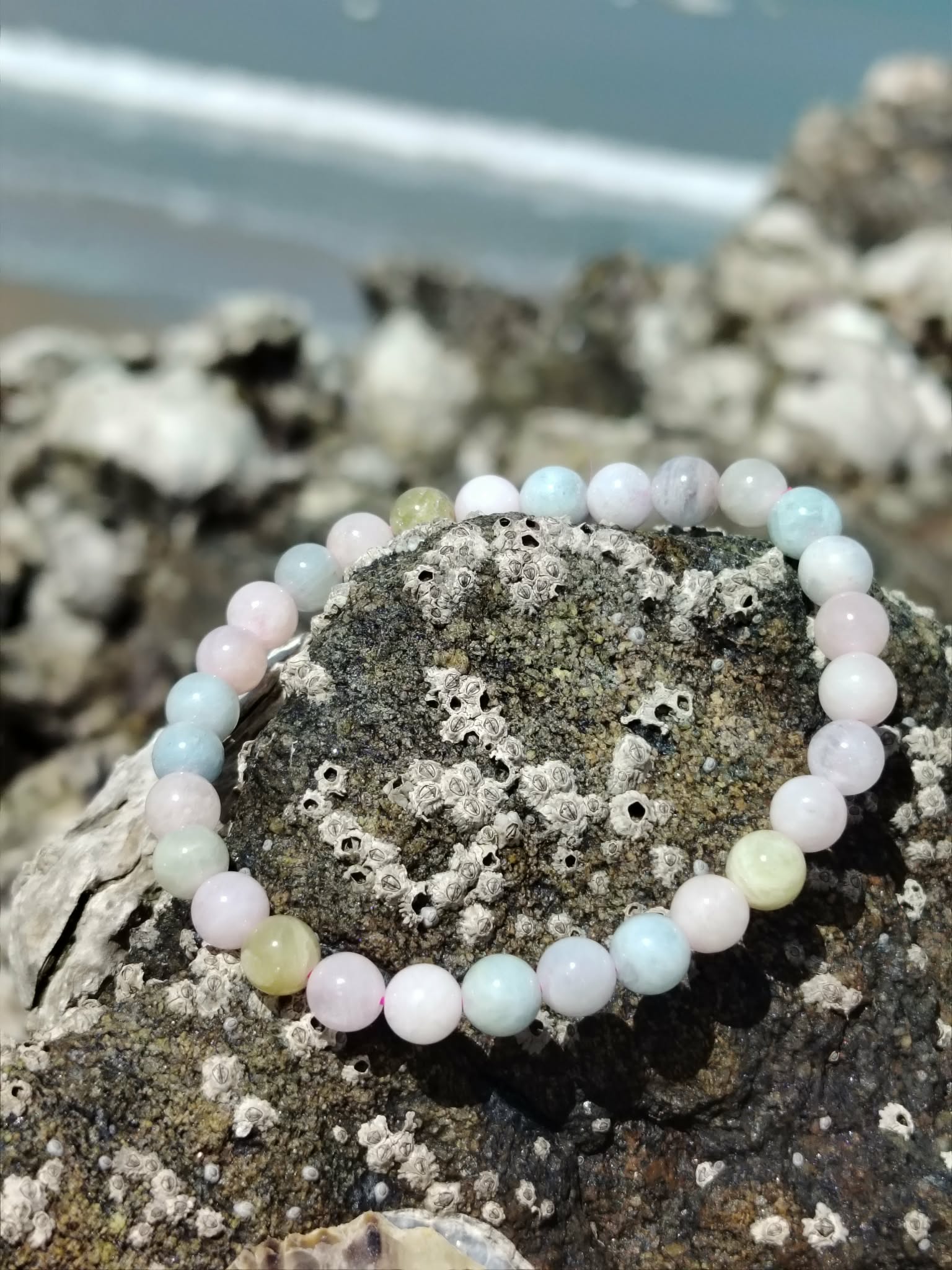 Bracelet Morganite 6 mm sur roche en bord de mer en Bretagne, perles pastel rose, bleu et vert d’eau, bijou en pierre naturelle associé à la douceur, à la paix intérieure et à l’harmonie du cœur.
