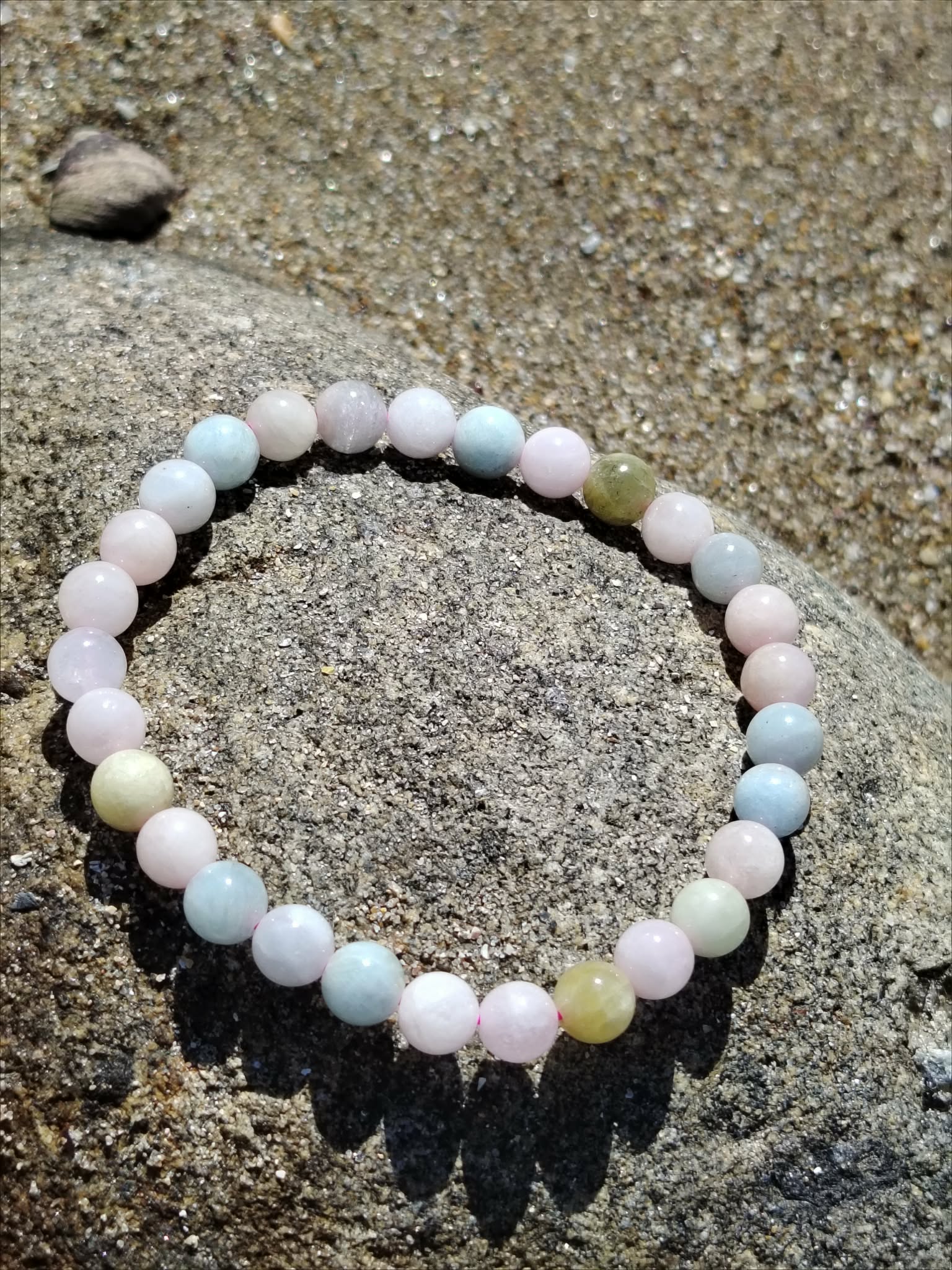 Bracelet Morganite 6 mm posé sur roche granitique en Bretagne, perles roses, bleues et vert d’eau en lumière naturelle, bijou en pierre naturelle associé à la sensibilité du cœur, au réconfort et à la sérénité.