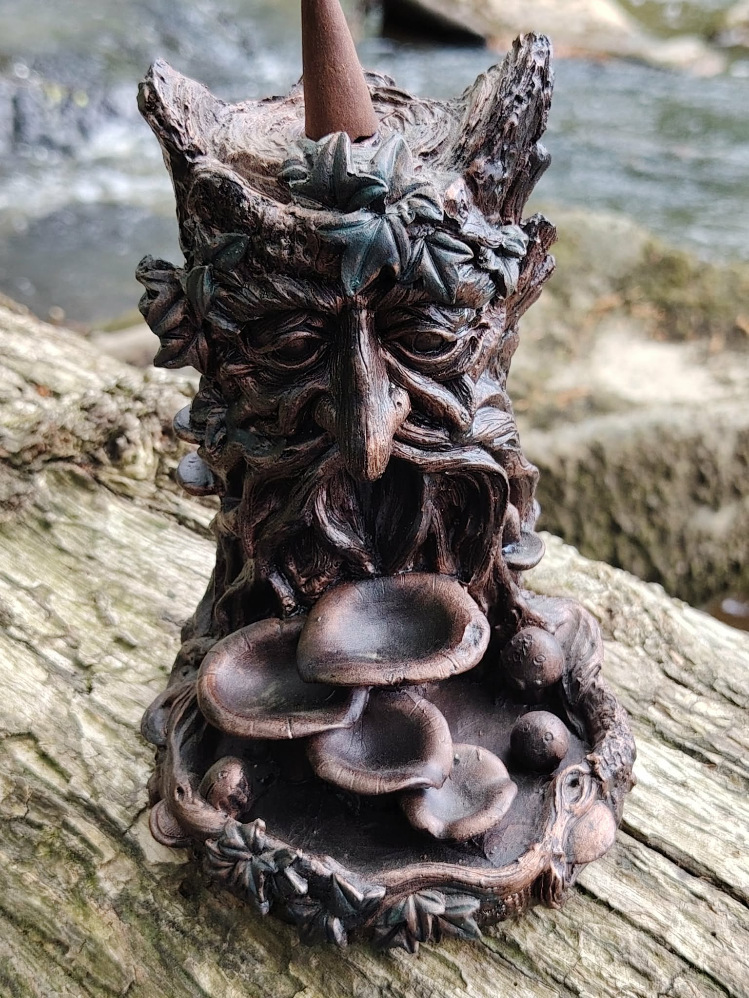 Brûleur d’encens à refoulement arbre en résine bronze posé sur mousse en forêt avec feuillage vert, visage sculpté et coupelles superposées pour effet cascade.
