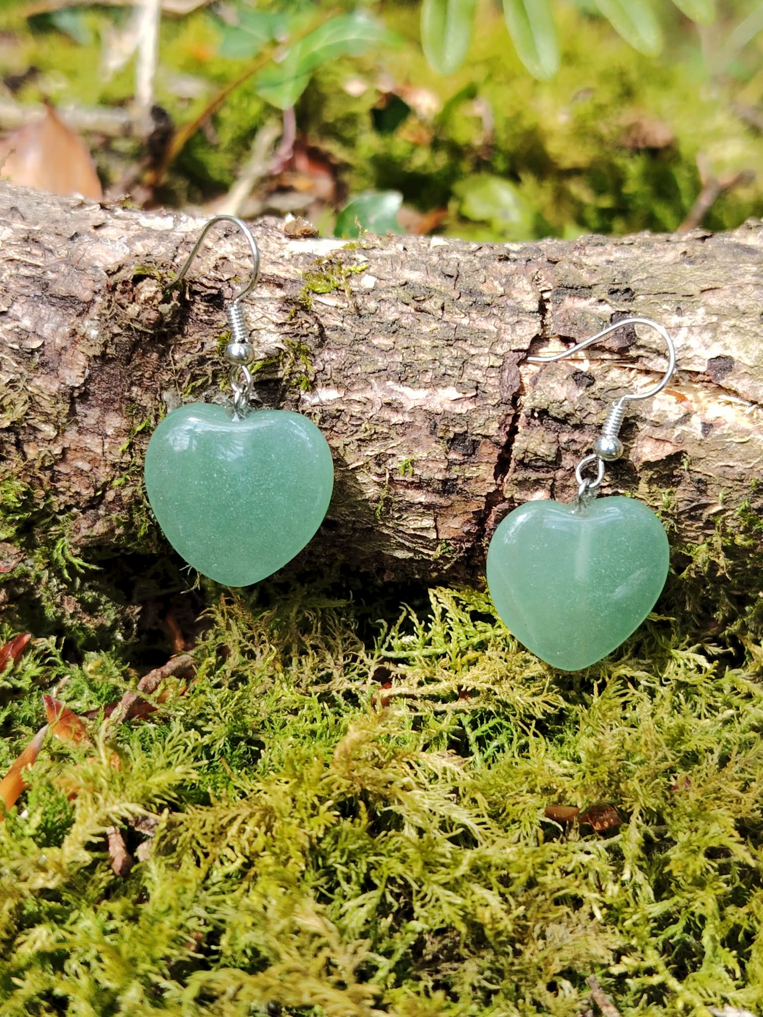 Boucles d’oreilles cœur en aventurine verte sur décor naturel, bijou en pierre naturelle associé à la douceur, à l’harmonie du cœur et à la sérénité intérieure.