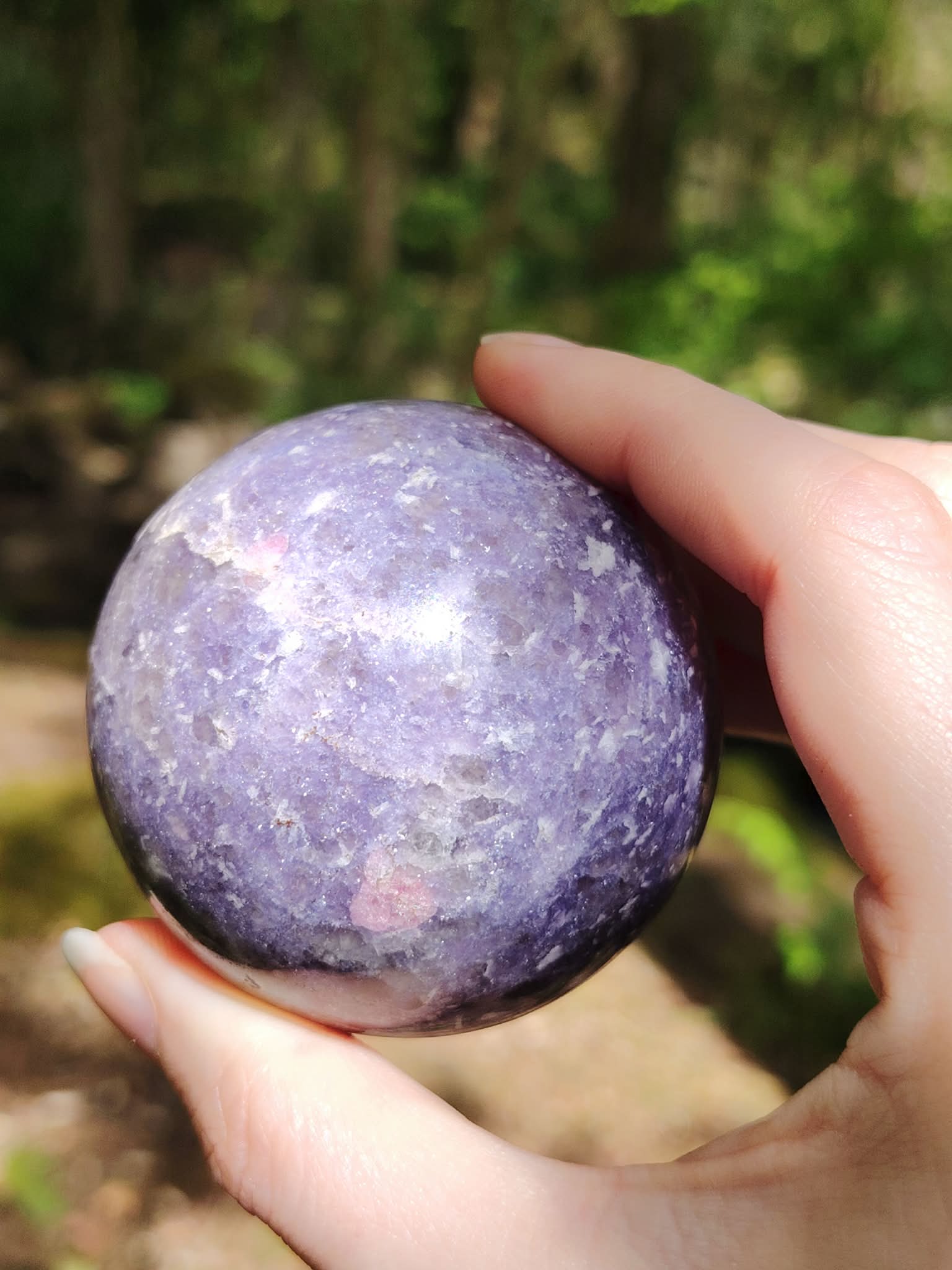 Sphère lépidolite tenue en main en forêt en Bretagne, pierre violette polie aux reflets doux, calme intérieur et équilibre émotionnel.