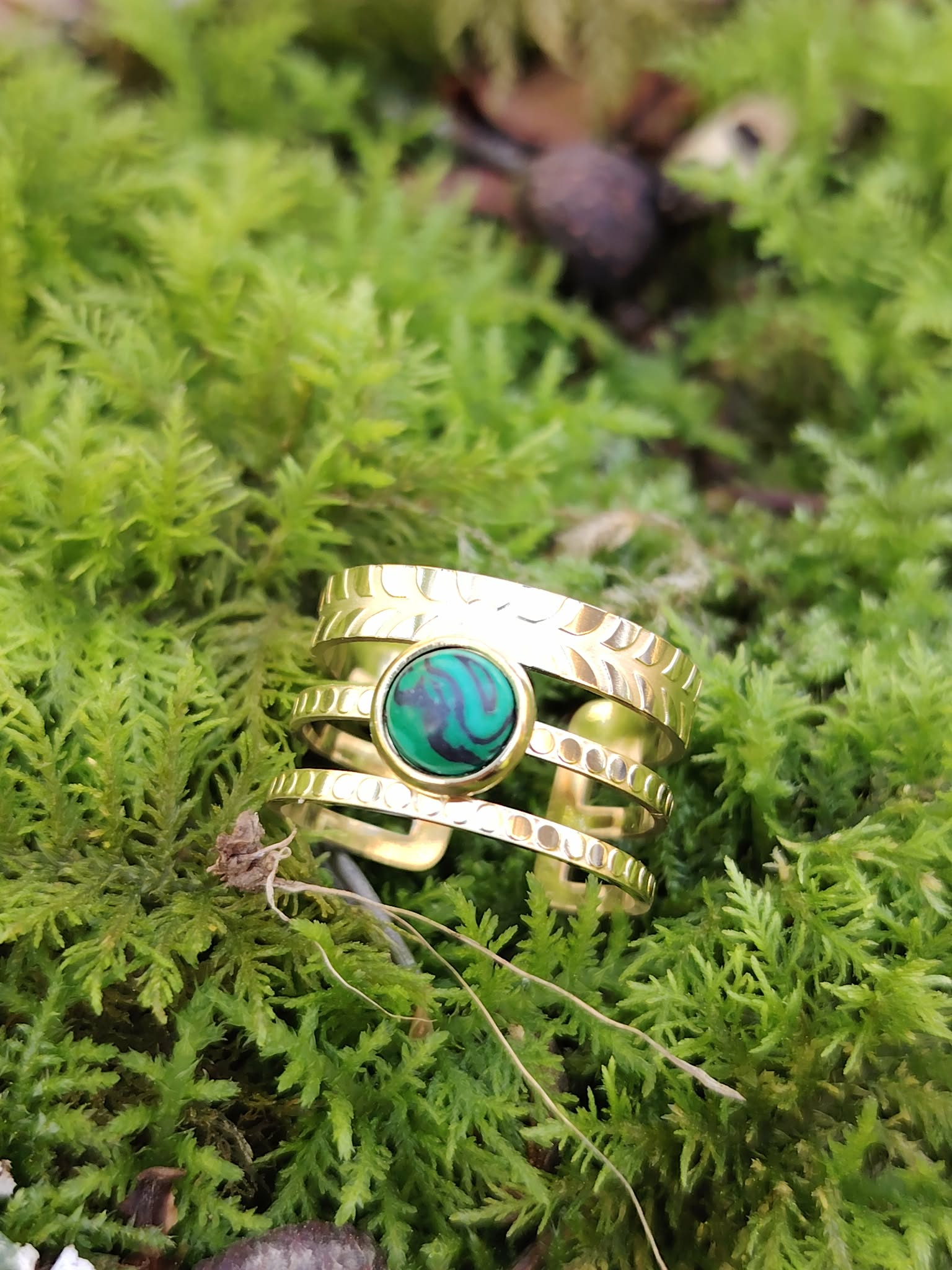 Bague dorée triple ligne avec pierre verte sur mousse en forêt, acier inoxydable ajustable et cabochon effet malachite, apaisement intérieur et élégance végétale.