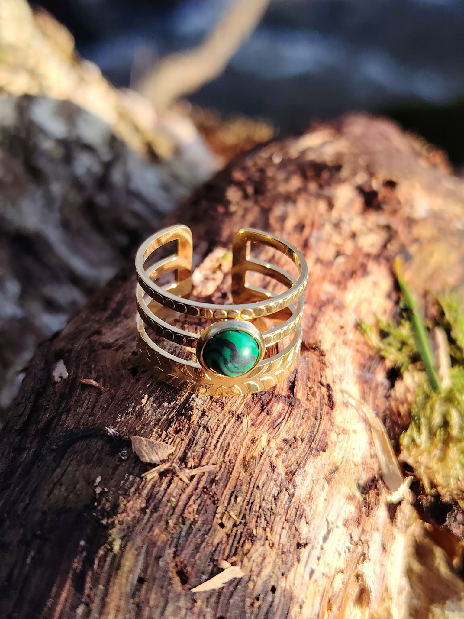 Bague ajustable dorée avec pierre verte sur souche en forêt, acier inoxydable brillant et pierre verte marbrée, stabilité émotionnelle et charme naturel.