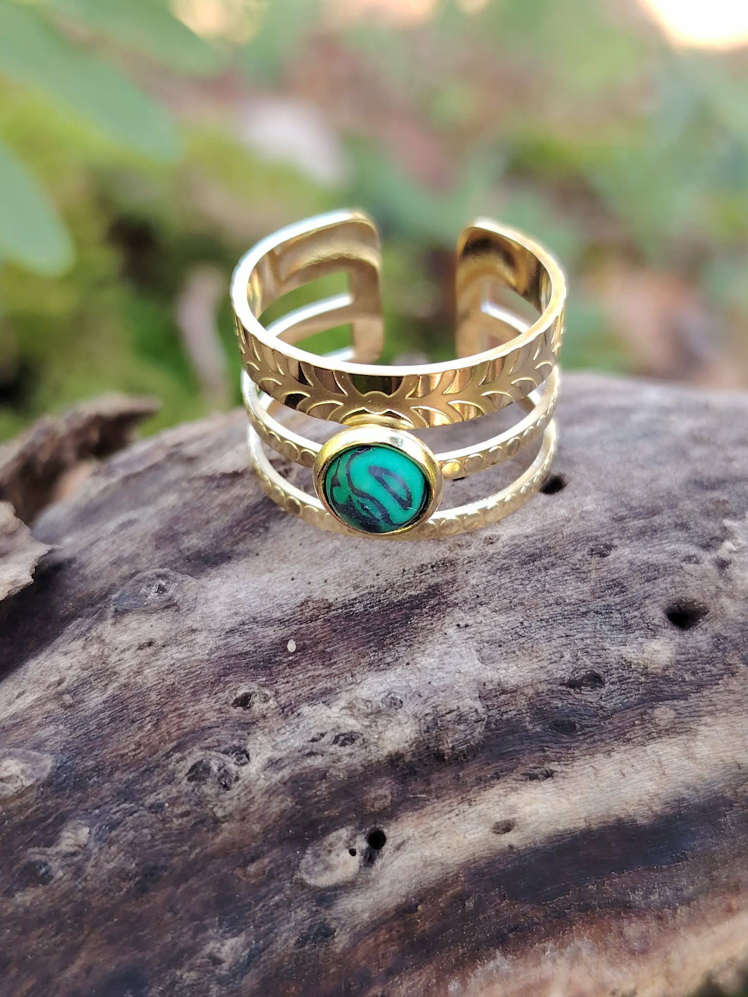 Bague pierre verte ajustable dorée sur bois naturel en extérieur, monture triple anneau et cabochon vert effet malachite, raffinement lumineux et sérénité.