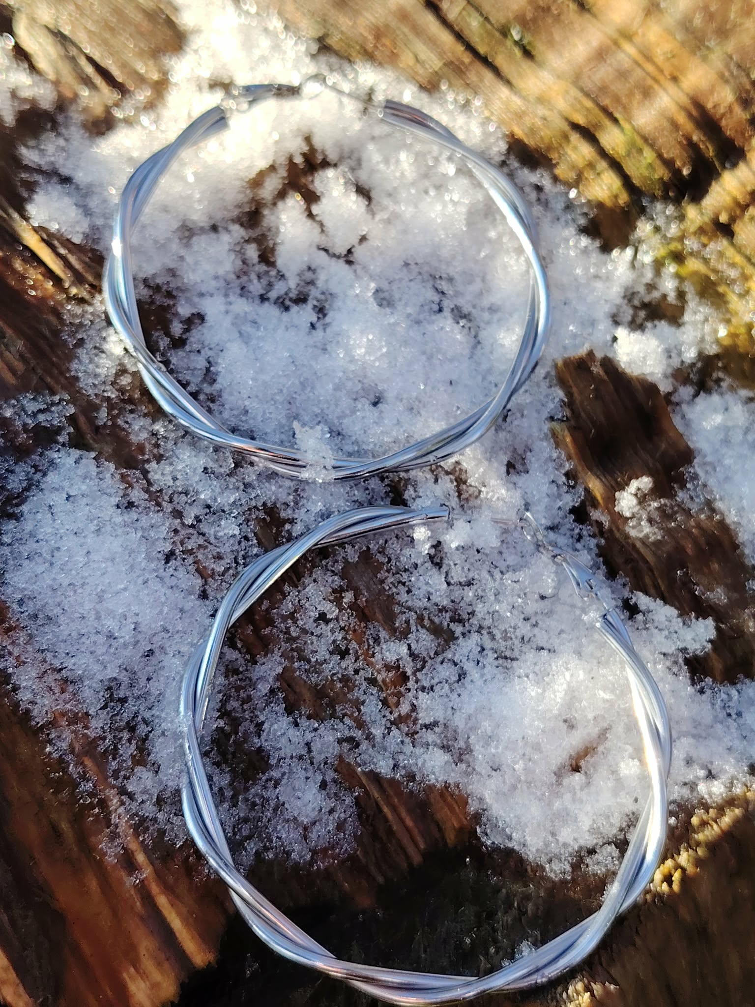Boucles d’oreilles créoles argentées torsadées sur bois et givre en extérieur, acier inoxydable lumineux, allure moderne et finition élégante.