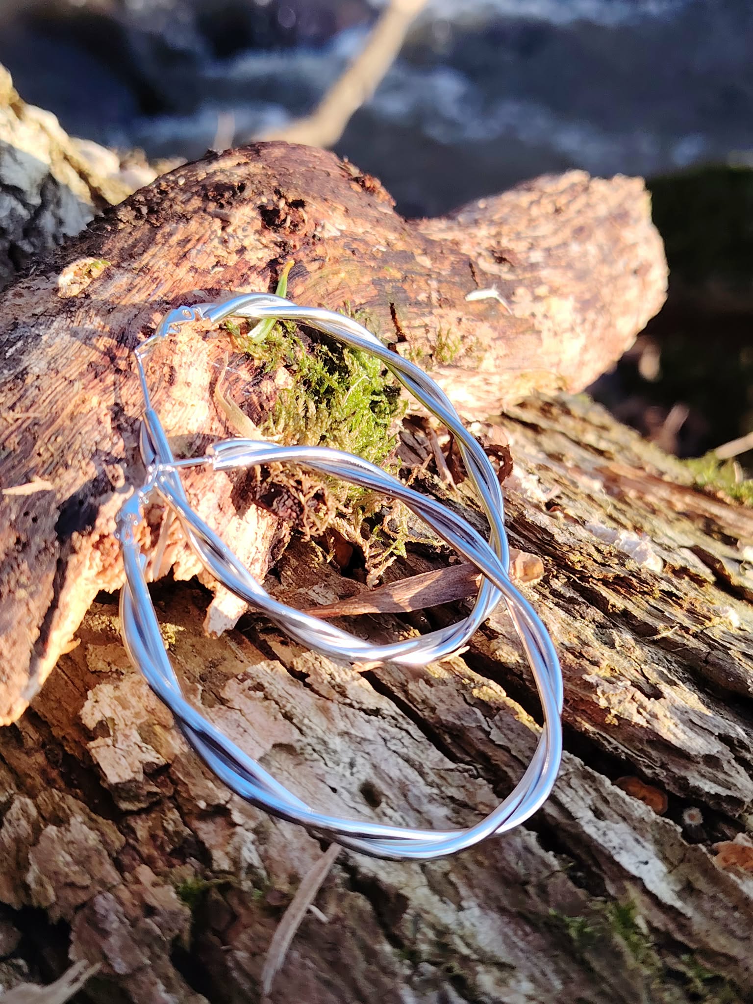 Créoles argentées effet torsadé lisse sur bois naturel au bord de mer en Bretagne, boucles d’oreilles en acier inoxydable au rendu moderne et épuré.