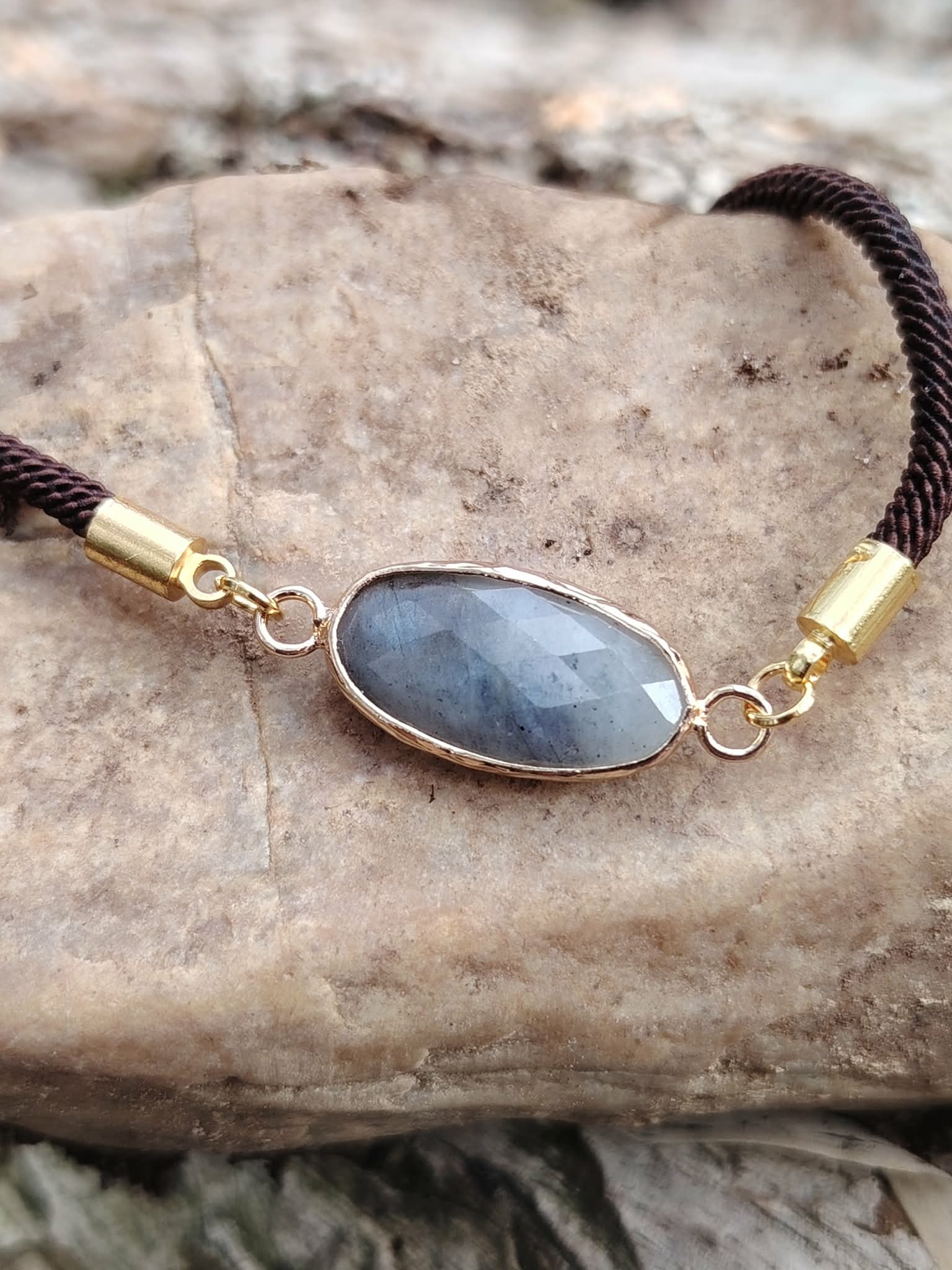Bracelet médaillon ovale facetté en labradorite en gros plan sur pierre naturelle, monture dorée et nuances gris ardoise, sérénité et élégance sobre.