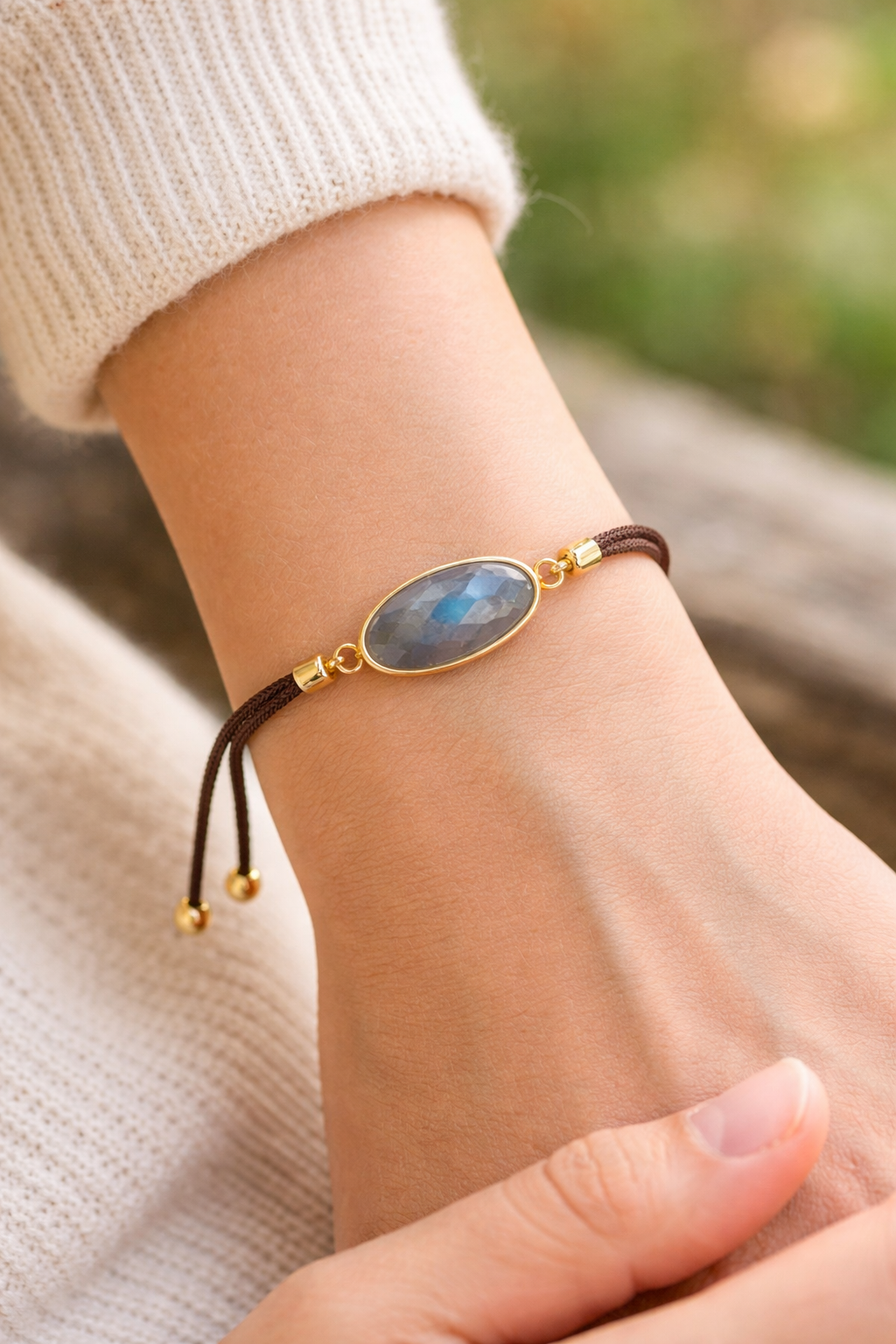 Bracelet médaillon ovale en labradorite facettée porté au poignet, cordon brun et reflets bleu gris de la pierre, clarté intérieure et style raffiné.