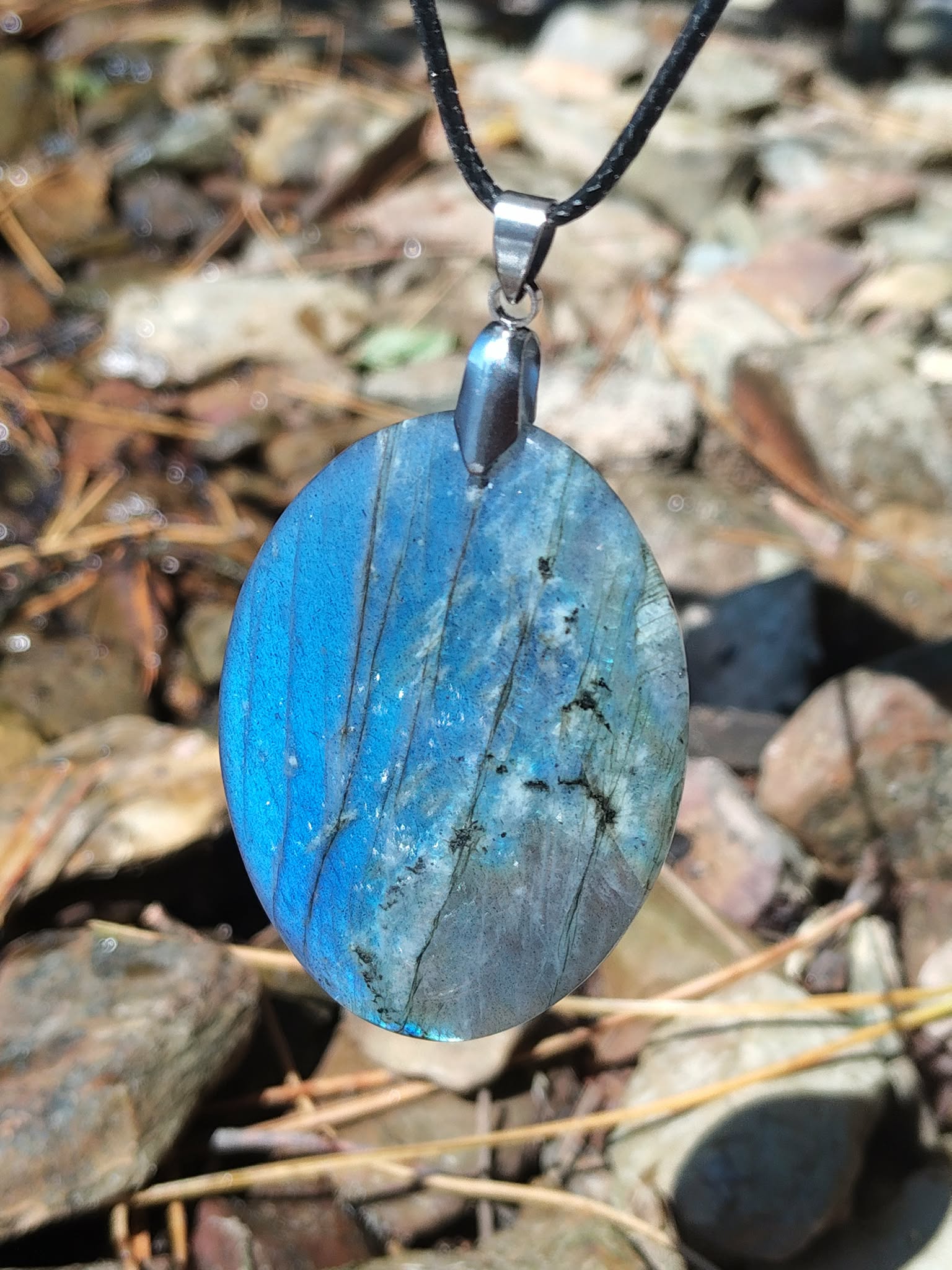 Pendentif ovale en labradorite aux reflets bleus tenu en main face à la mer en Bretagne, pierre naturelle polie et bélière argentée, apaisement du mental et intuition.