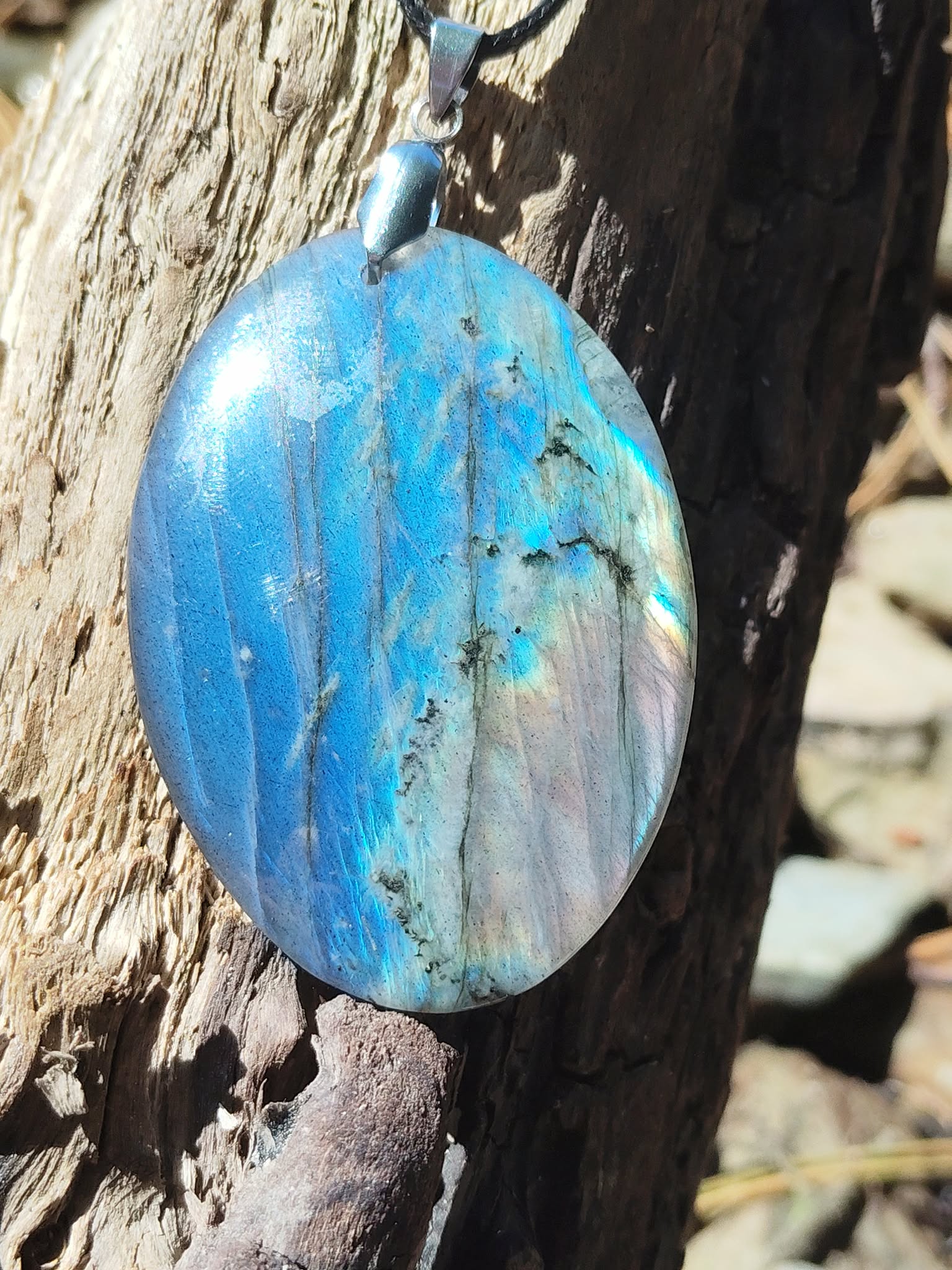 Pendentif ovale en labradorite photographié sur roche marine bretonne, éclats bleu lagon et vert doré sur pierre polie avec attache argentée, intuition éveillée et ancrage subtil.