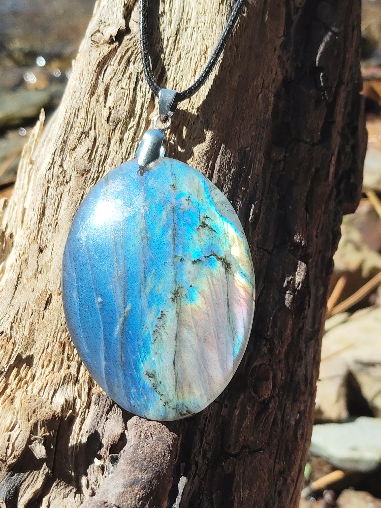 Zoom sur pendentif ovale en labradorite aux reflets bleus sur pierre naturelle en décor breton, bélière argentée et éclats irisés, clarté mentale et stabilité émotionnelle.