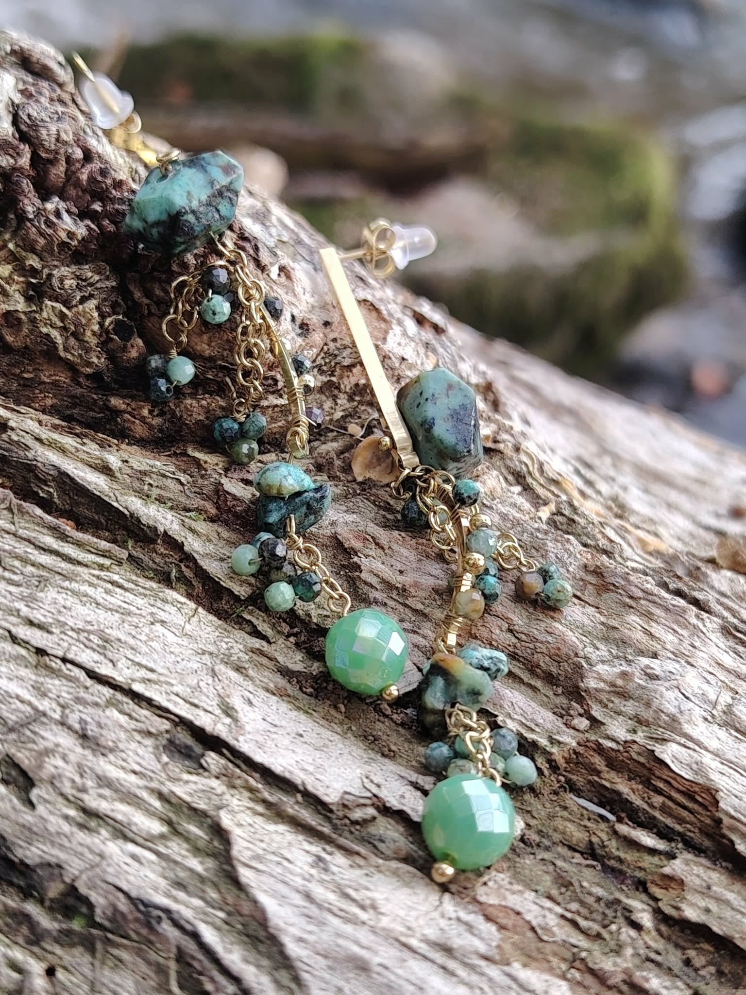 Boucles d’oreilles dorées en turquoise africaine posées sur écorce naturelle, pampilles de perles vertes facettées et éclats minéraux, sérénité intérieure et style raffiné.