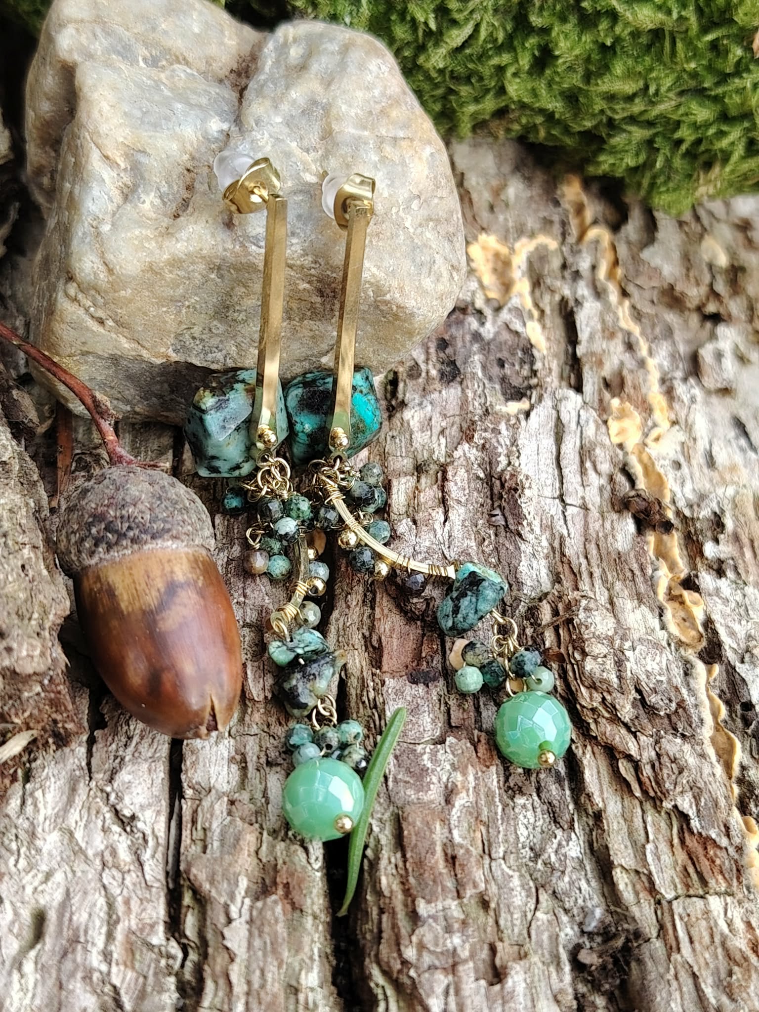 Boucles d’oreilles turquoise africaine et métal doré sur bois brut avec gland et mousse, perles facettées vert tendre et pierres marbrées, équilibre intérieur et charme naturel.