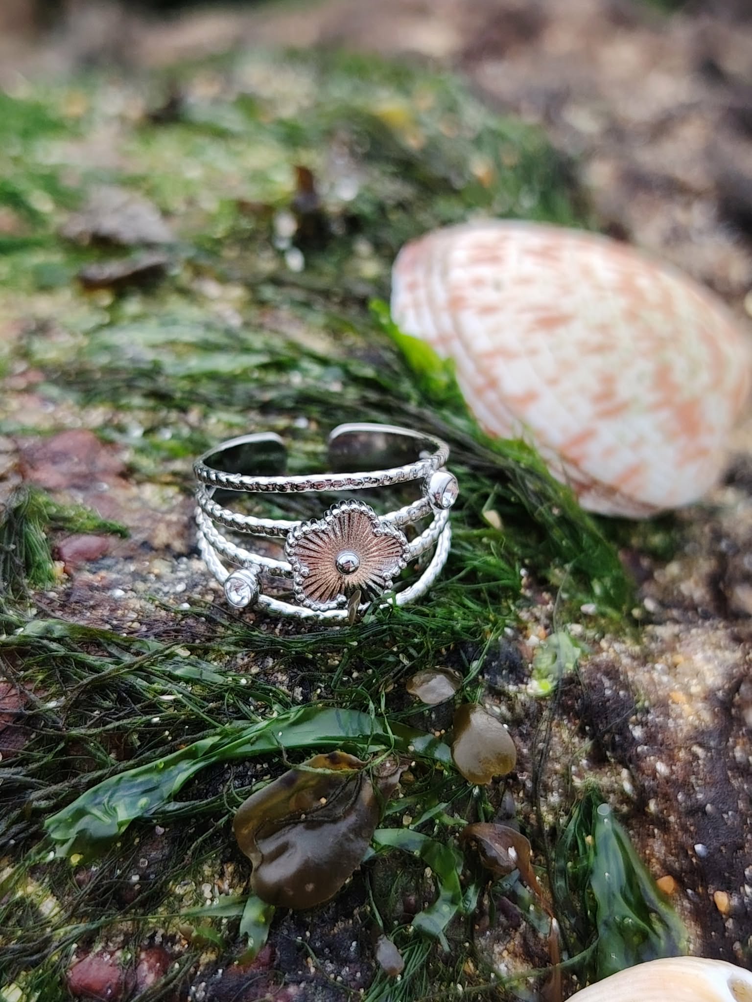 Bague fleur argentée ajustable sur fond blanc, acier inoxydable brillant avec anneaux texturés et strass discrets, allure élégante et féminine.