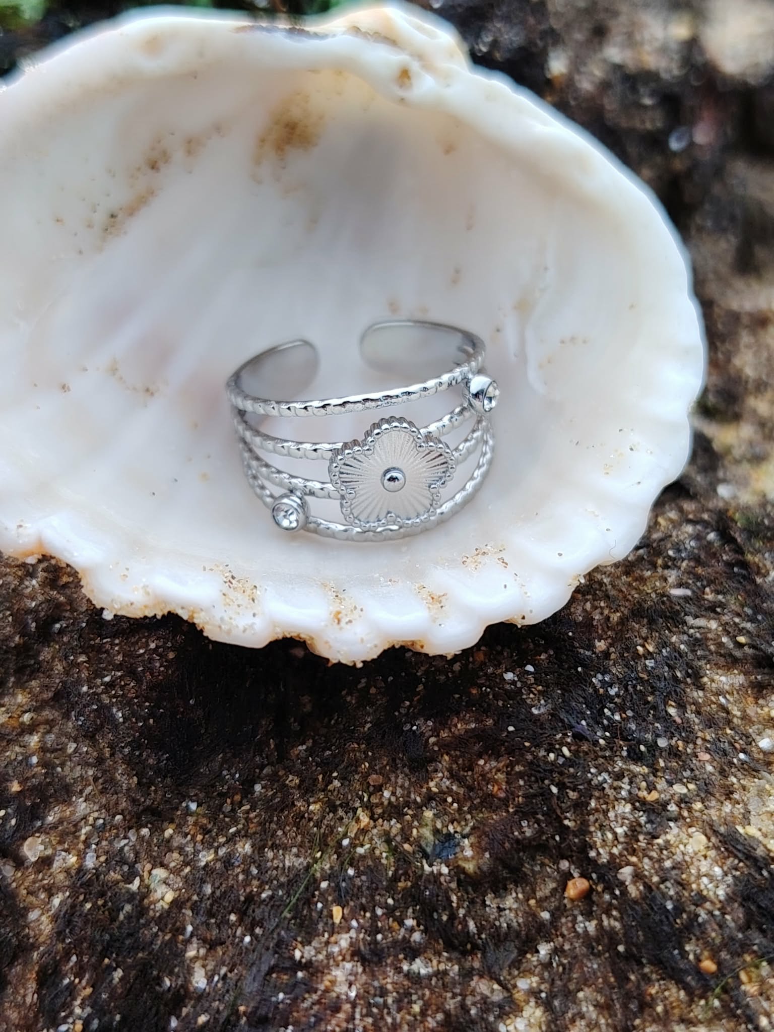 Bague ajustable argentée fleur avec strass sur bois naturel en extérieur, acier inoxydable éclatant et design floral ajouré, élégance discrète au quotidien.