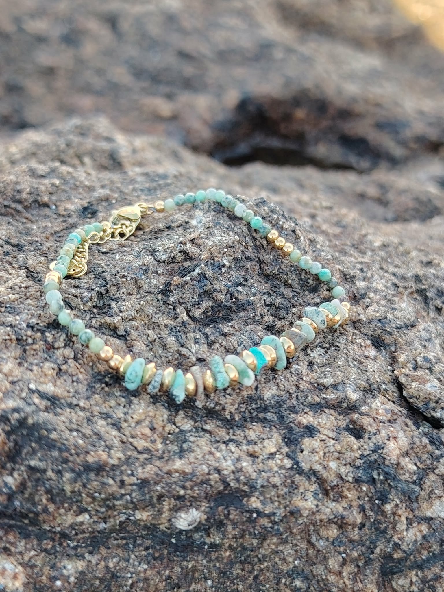 Zoom sur bracelet doré turquoise africaine et perles vert sauge sur roche naturelle en Bretagne, détails fins et teintes minérales, harmonie et apaisement intérieur.