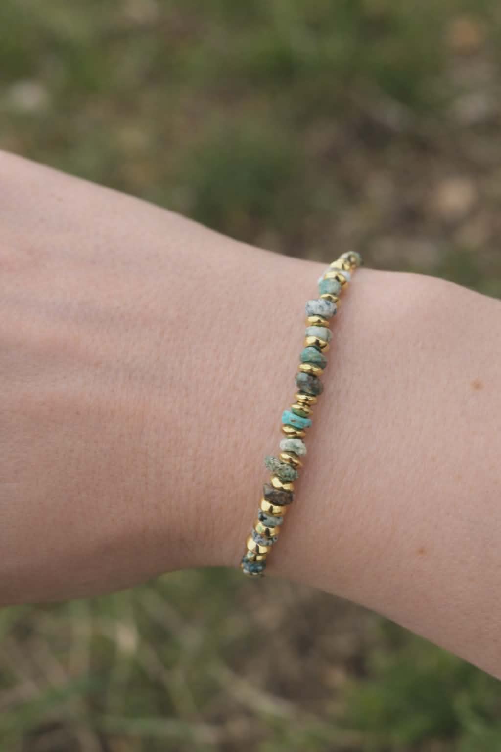 Bracelet doré en turquoise africaine photographié sur mousse en forêt, perles vert sauge et bleu minéral, sérénité intérieure et élégance naturelle.