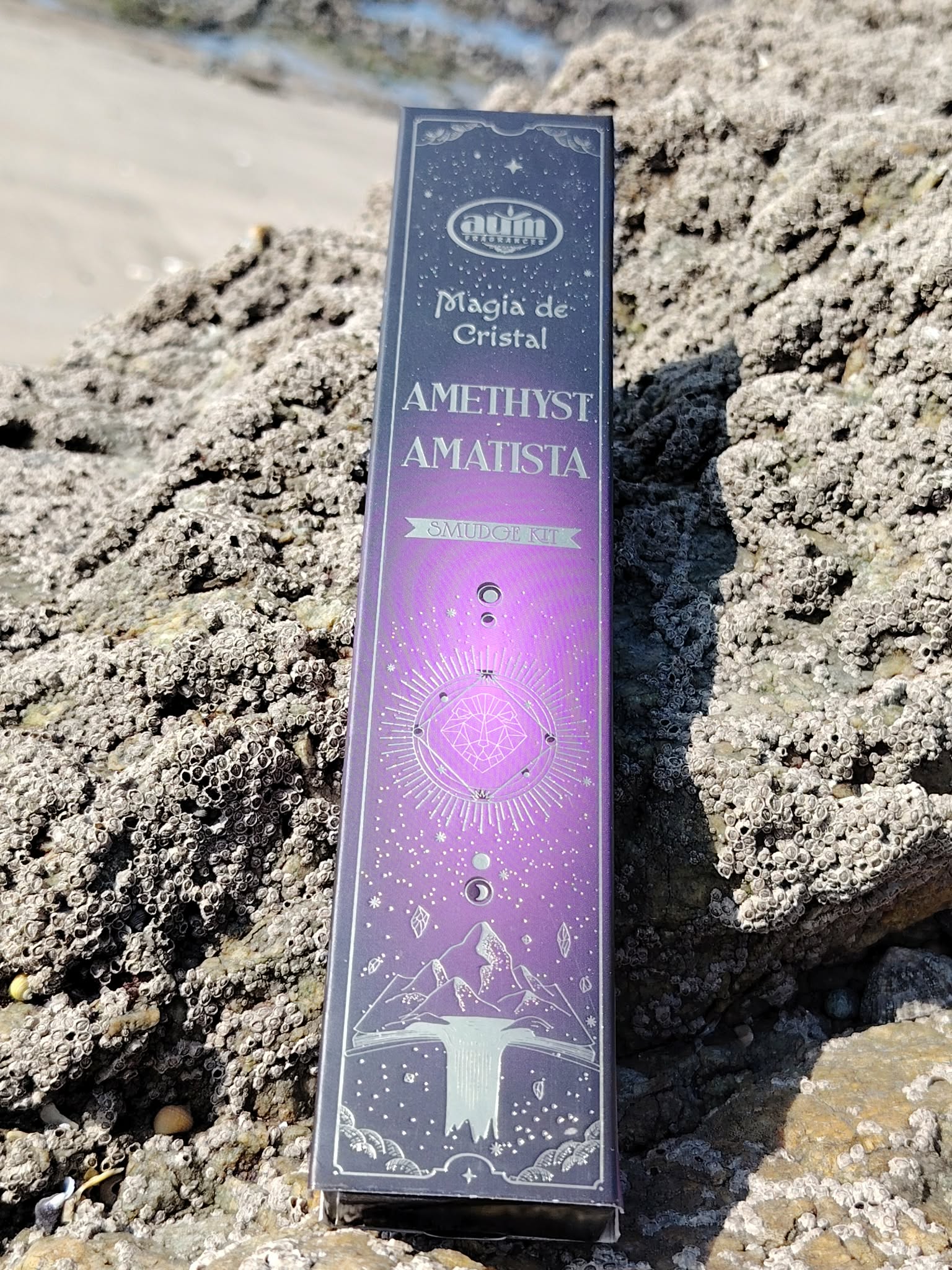 Boîte d’encens améthyste Aum Crystal Magic photographiée sur rochers au bord de mer en Bretagne, coffret violet lumineux, parfum d’intérieur et moment apaisant.