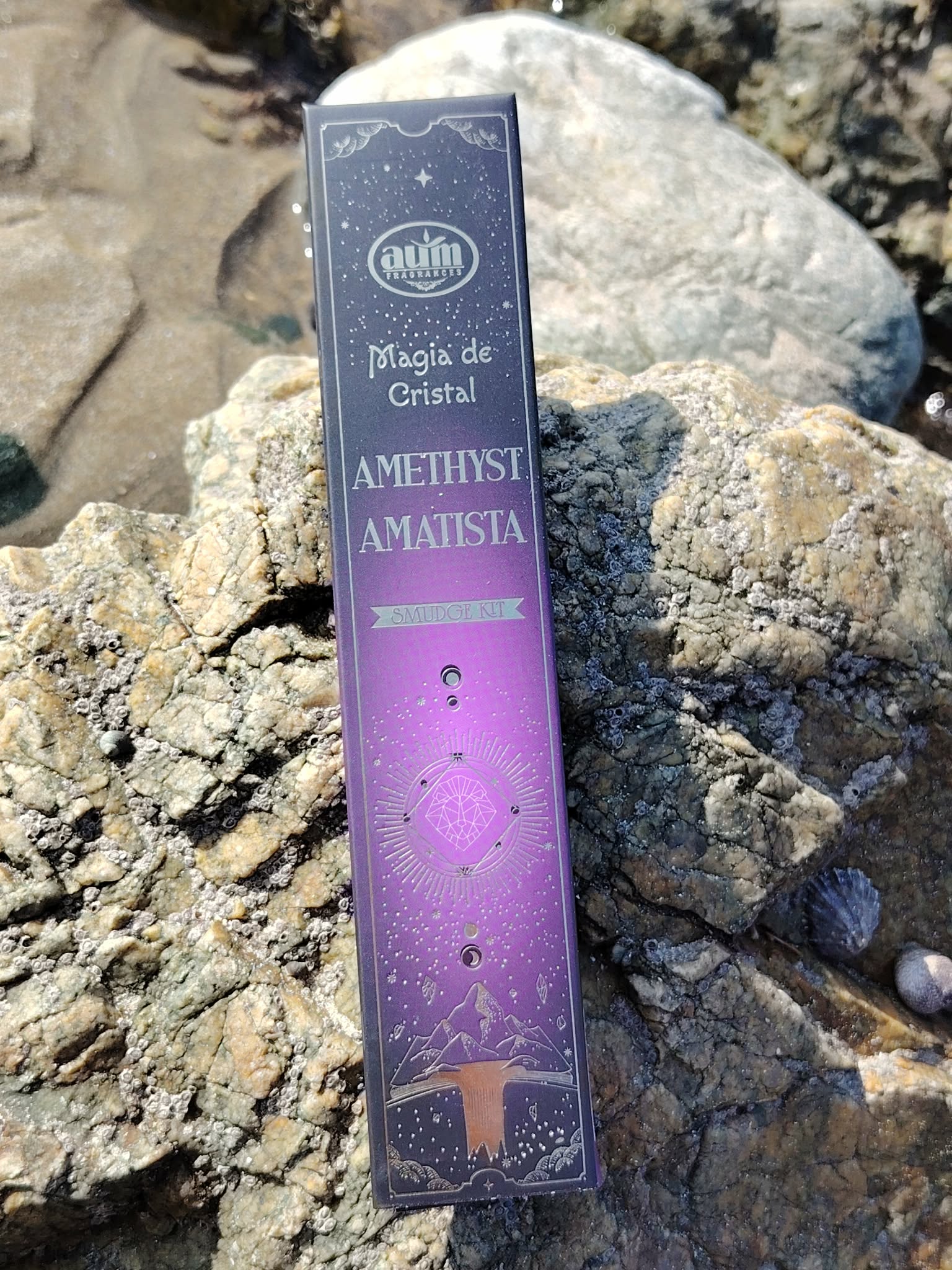 Boîte d’encens améthyste Aum Crystal Magic 20 g sur rochers au bord de mer en Bretagne, coffret violet lumineux, parfum d’intérieur et moment apaisant.