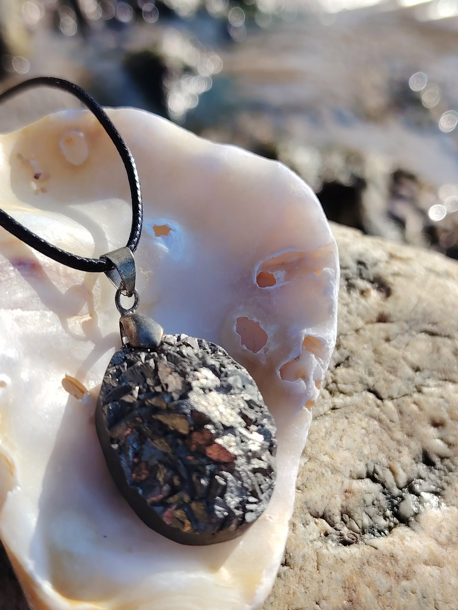 Pendentif pyrite naturelle sur coquillage au bord de mer en Bretagne, pierre sombre aux reflets cuivrés et argentés, favorisant l’ancrage et la solidité émotionnelle.