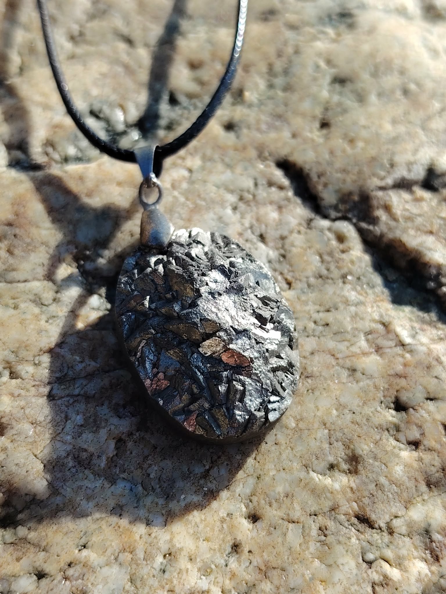 Pendentif pyrite naturelle ovale sur coquillage clair en bord de mer en Bretagne, pierre métallisée argentée montée sur cordon noir, soutien de la protection et de la confiance en soi.