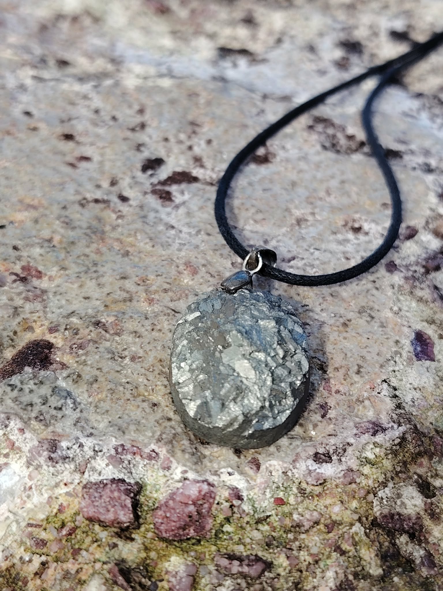 Pendentif pyrite naturelle posé en extérieur en Bretagne, pierre brillante argentée sur cordon noir, pierre de protection douce et de confiance personnelle.