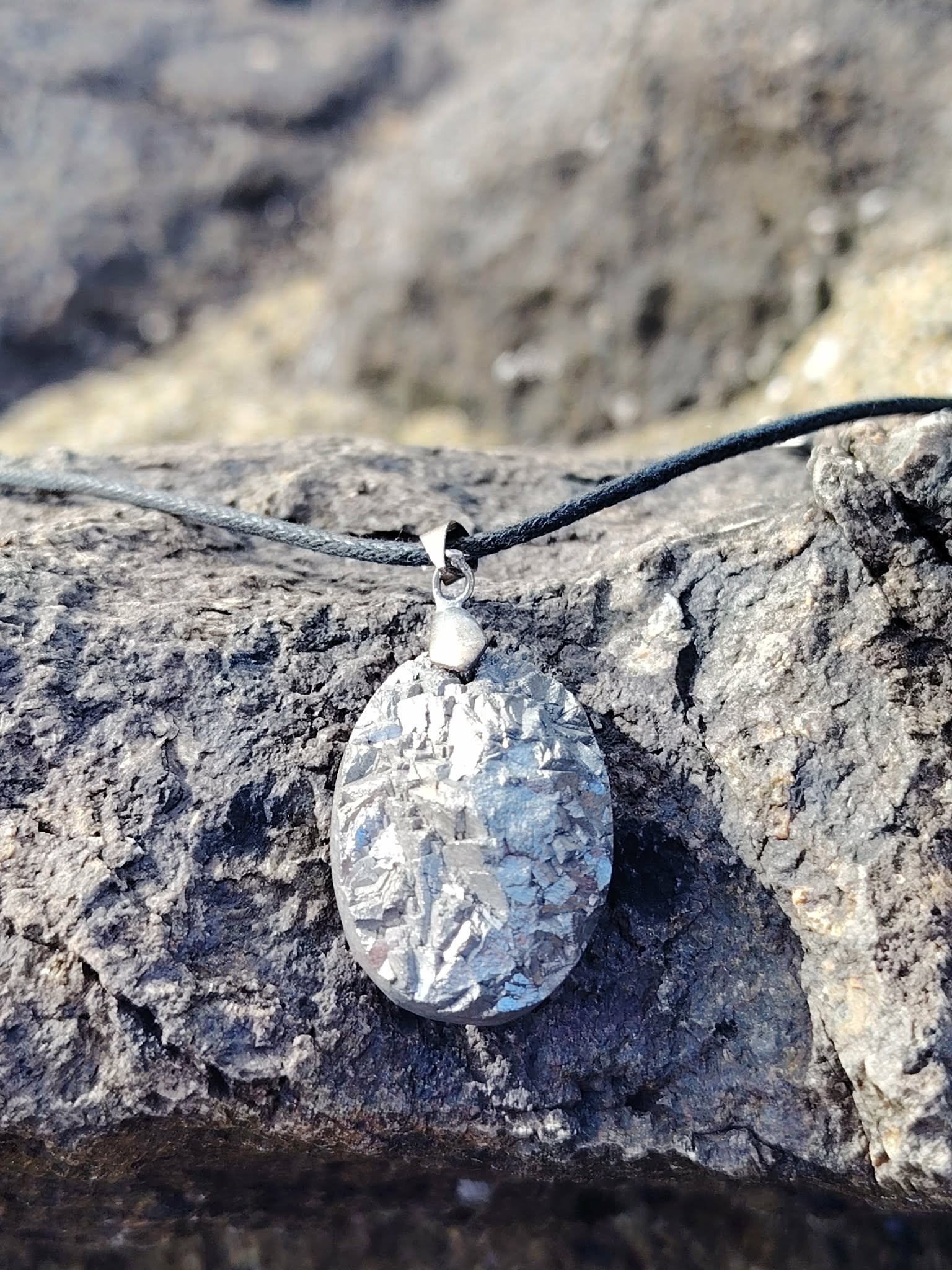 Pendentif pyrite naturelle sur roche au bord de mer en Bretagne, pierre argentée brillante montée sur cordon noir, associée à la stabilité et à l’assurance.