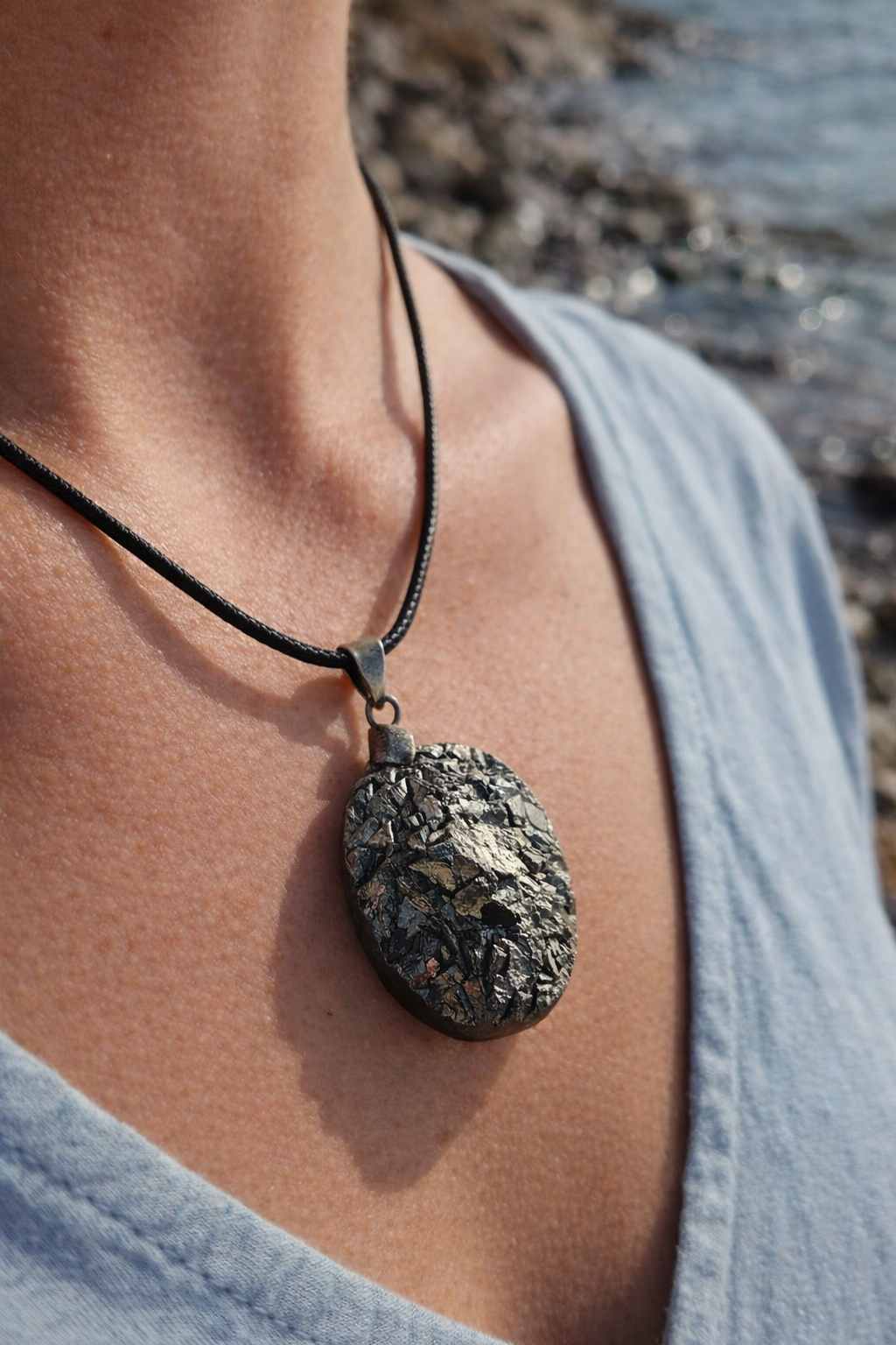 Pendentif pyrite naturelle porté au cou en extérieur en Bretagne, pierre aux reflets métalliques sur cordon noir, alliée de l’ancrage et de la force intérieure.