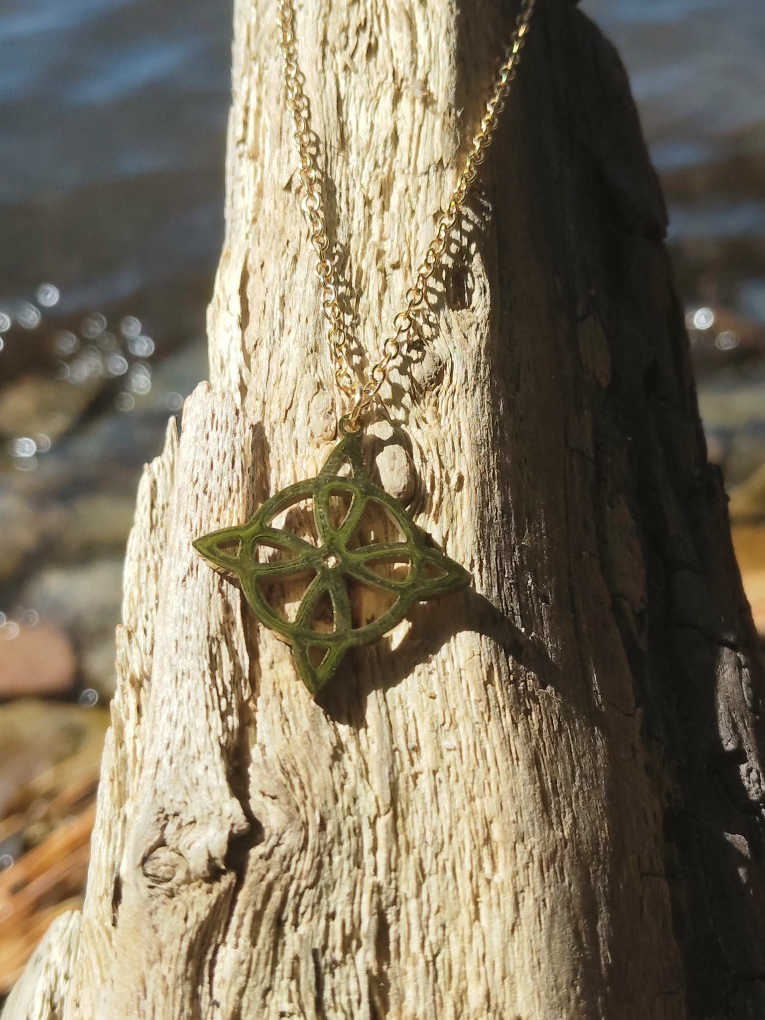 Pendentif nœud de sorcière doré sur décor naturel, bijou de protection spirituelle inspirant confiance et recentrage.