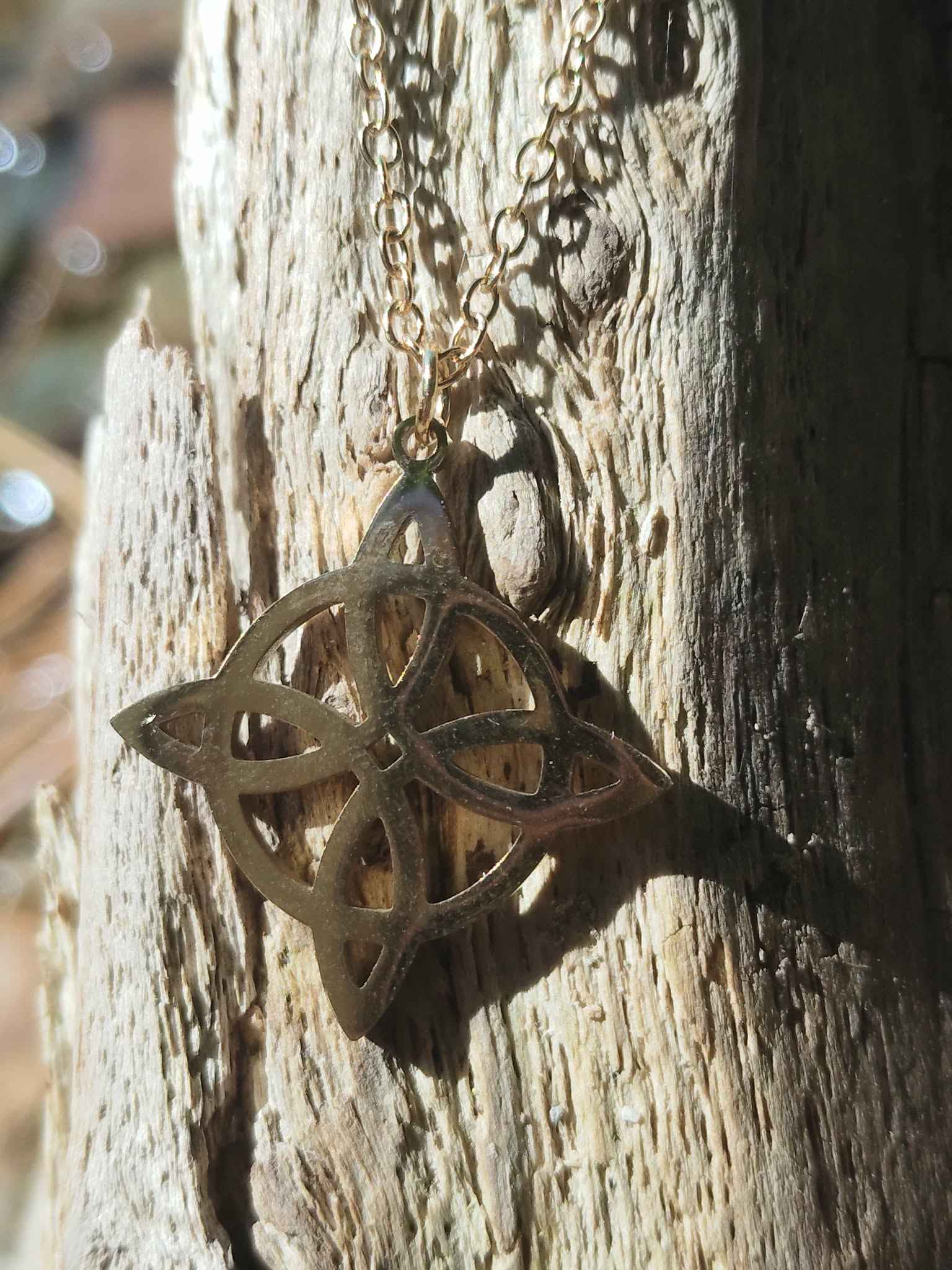 Pendentif nœud de sorcière doré en acier inoxydable sur fond doux, symbole ésotérique d’harmonie, de protection et de solidité intérieure.