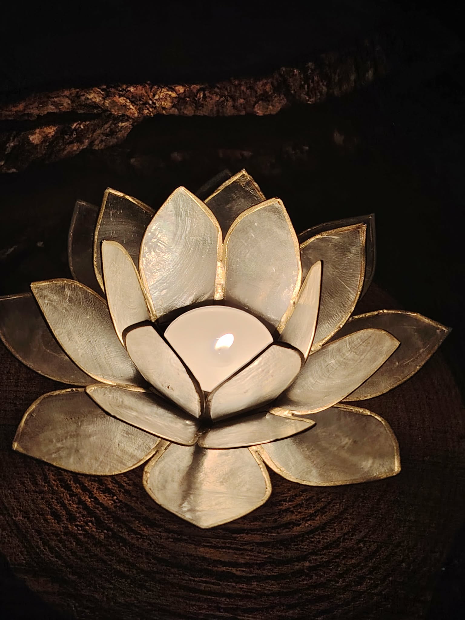Photophore lotus nacré doré allumé dans une ambiance sombre, bougeoir lotus en coquilles de Capiz pour lumière douce et zen.