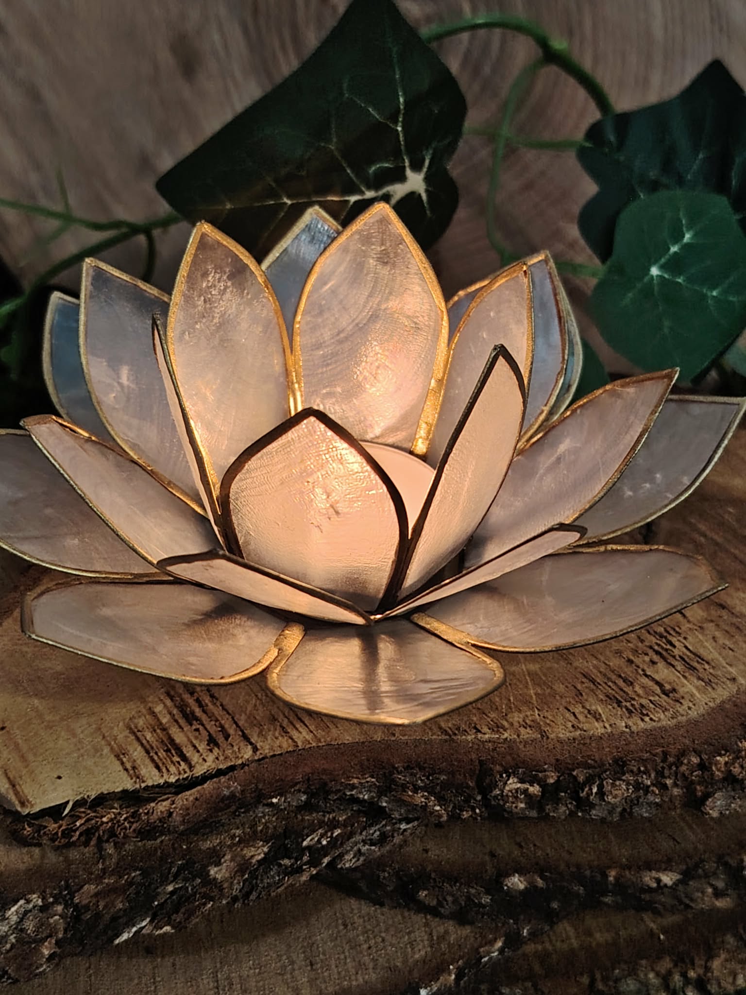 Photophore lotus nacré doré éclairé sur support en bois naturel, fleur lotus lumineuse pour autel, méditation et décoration apaisante.