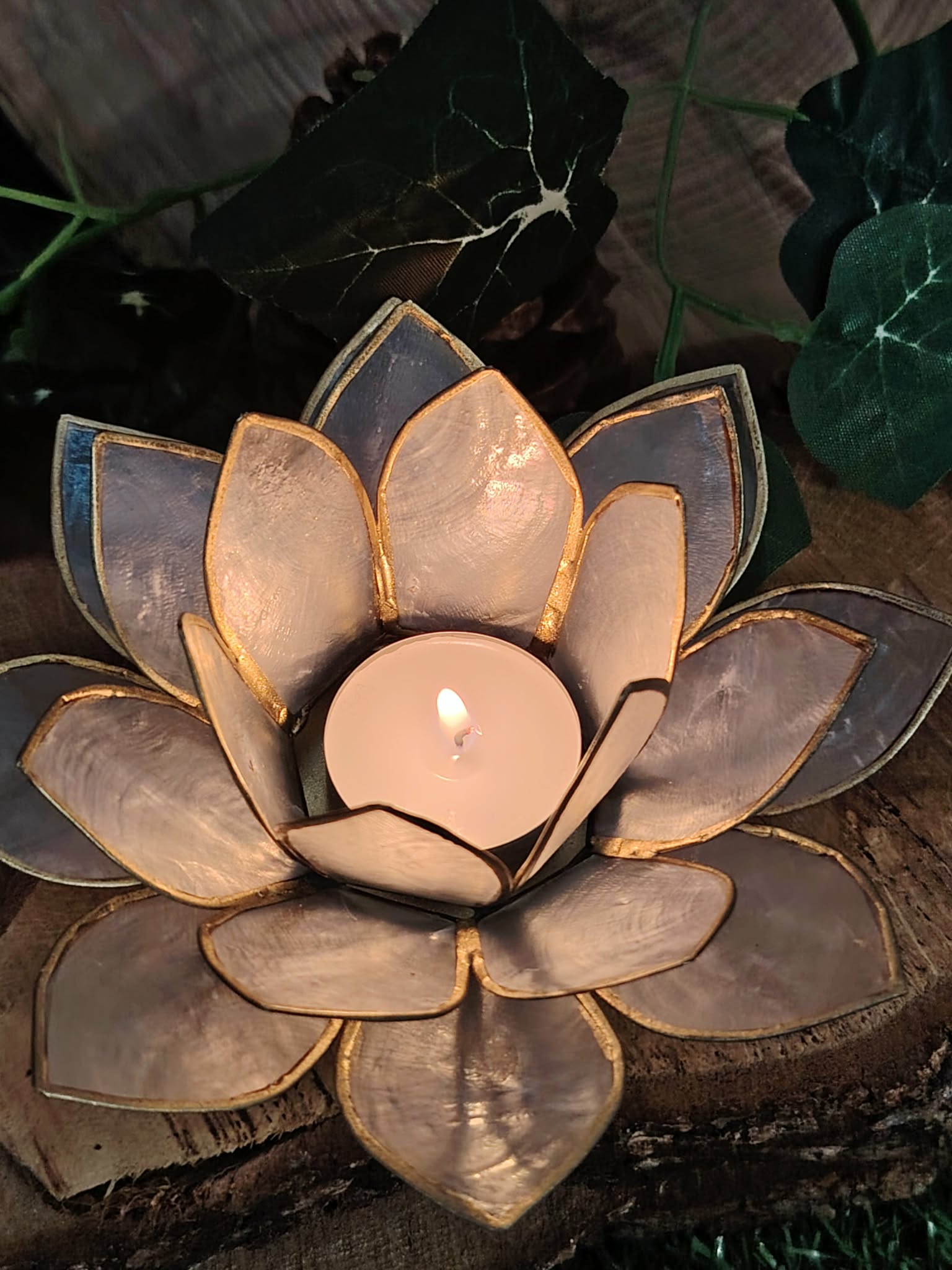 Photophore lotus nacré doré avec bougie chauffe-plat sur décor bois et feuillage, objet zen lumineux aux reflets nacrés.